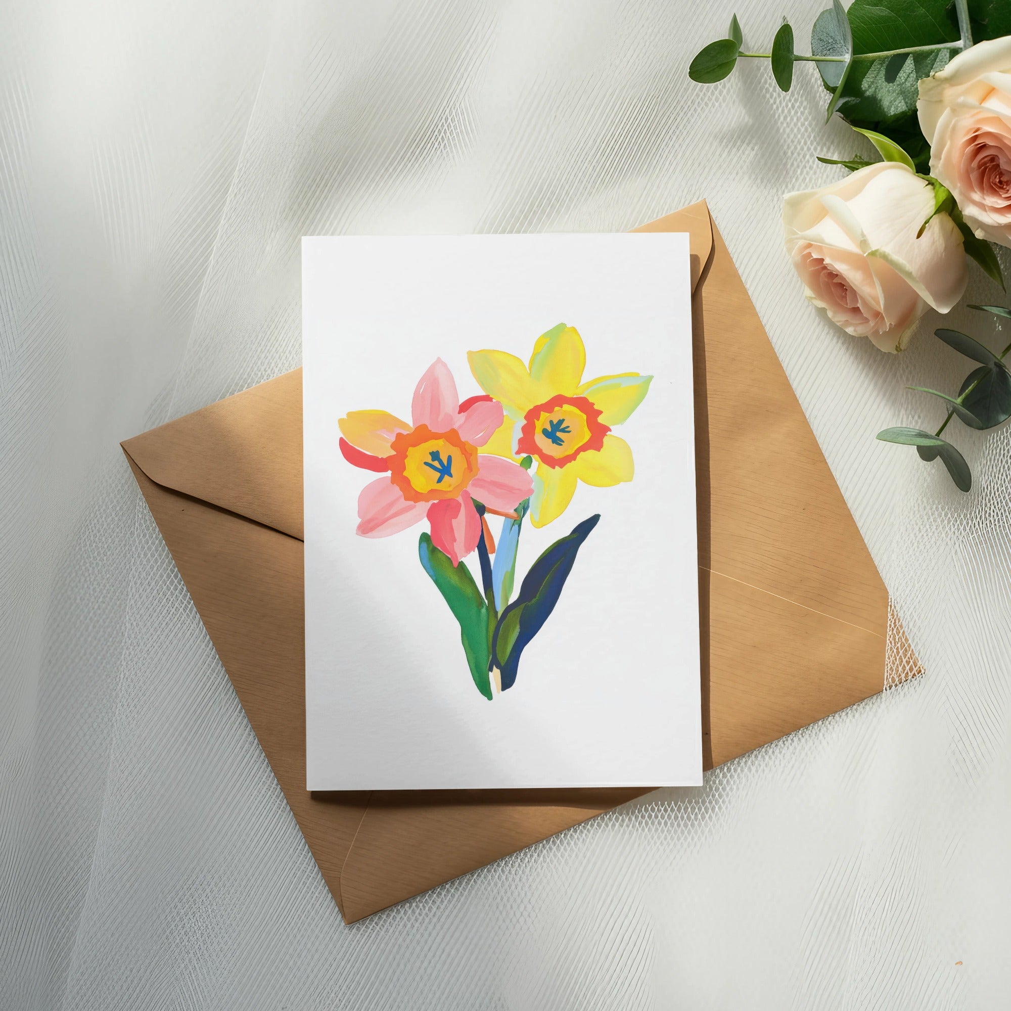 Watercolor painting of pink and yellow daffodils on a card, with an envelope and roses.