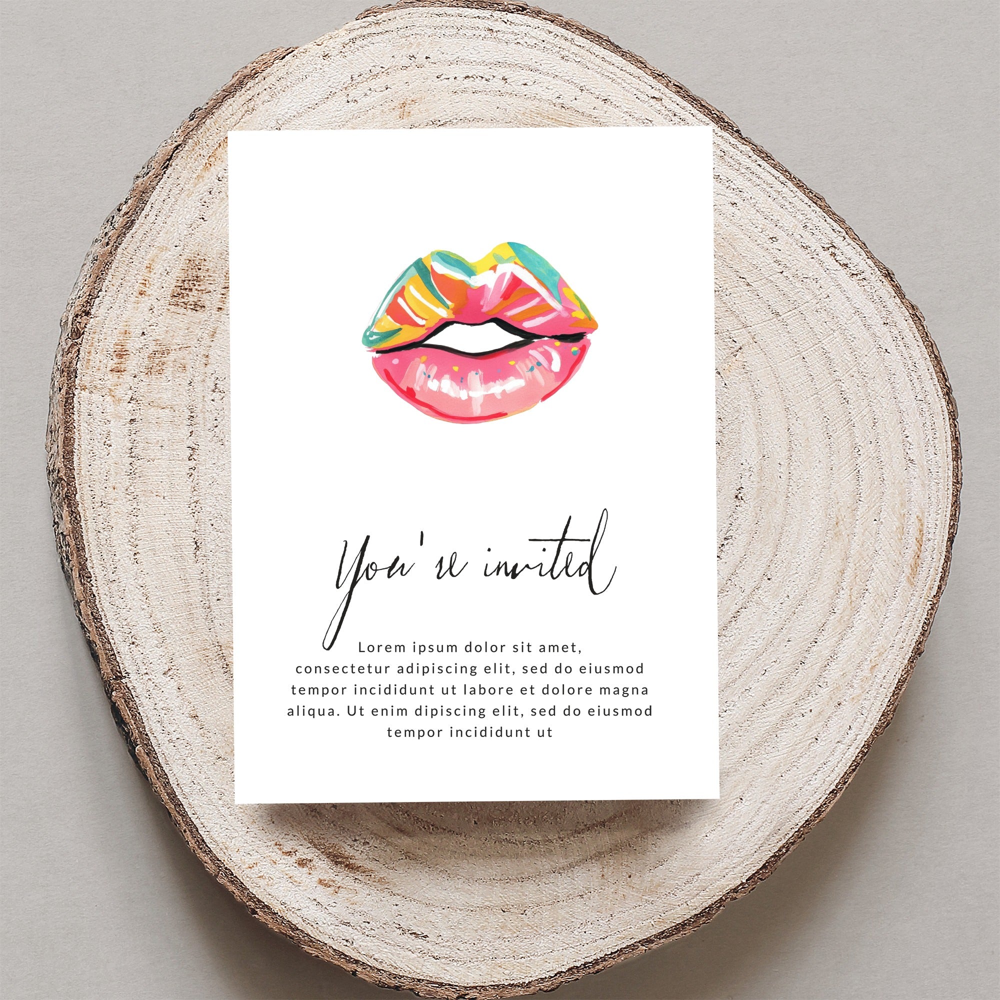 Card with "You're invited" and lips illustration, on wood slice.