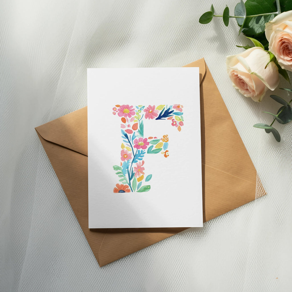 Watercolor letter F with floral accents on a card atop a kraft envelope.