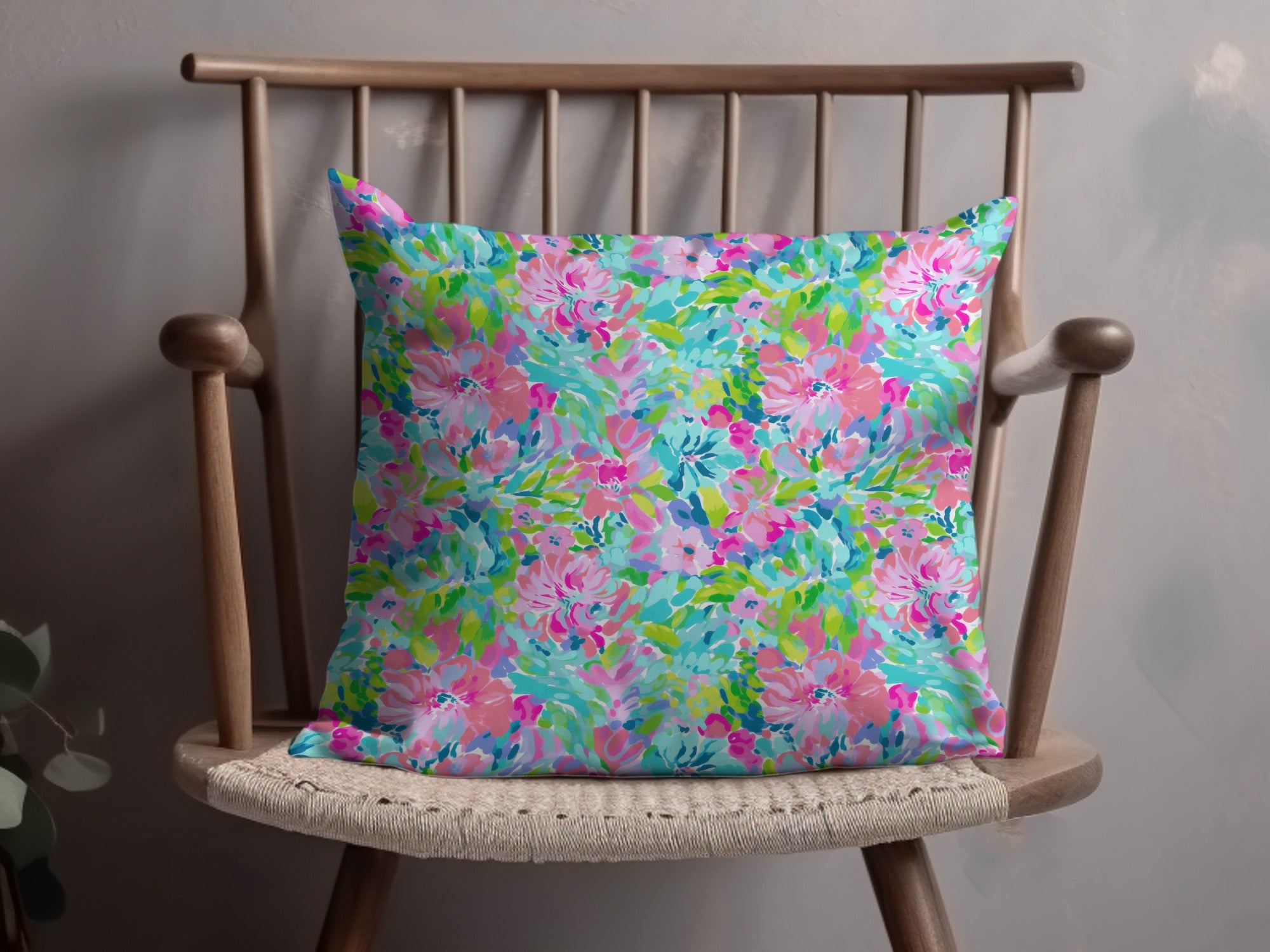 Floral throw pillow with pink, blue, and green watercolor design on a wooden chair.