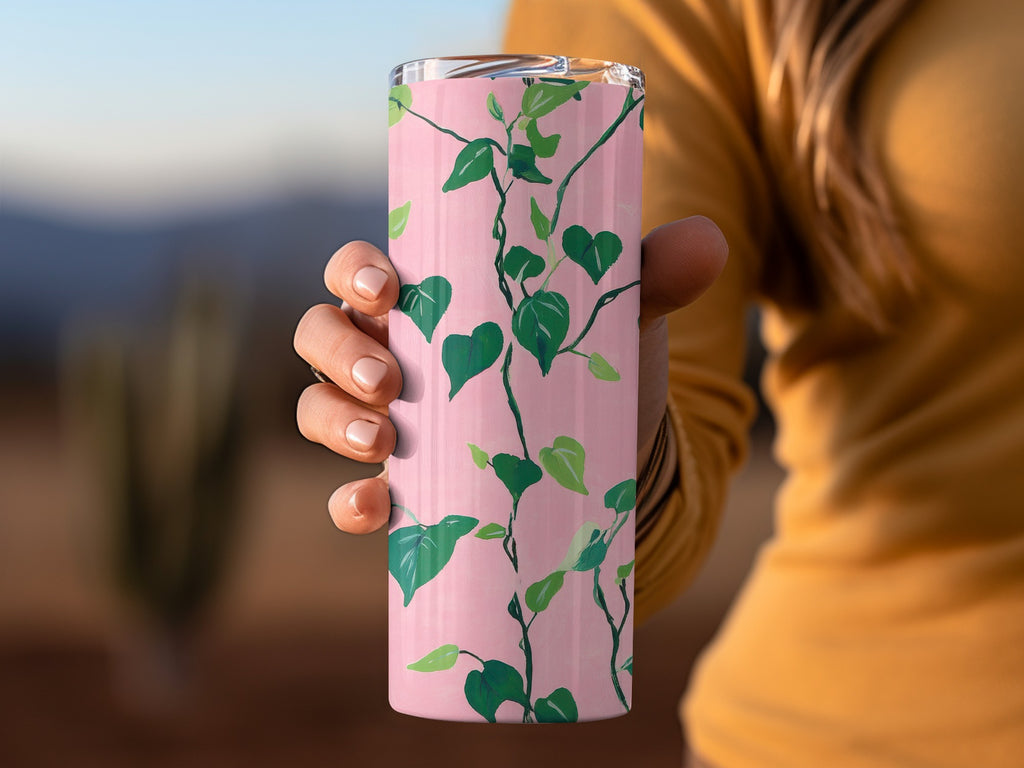 Pink tumbler with a green vine and leaf pattern held by a hand.