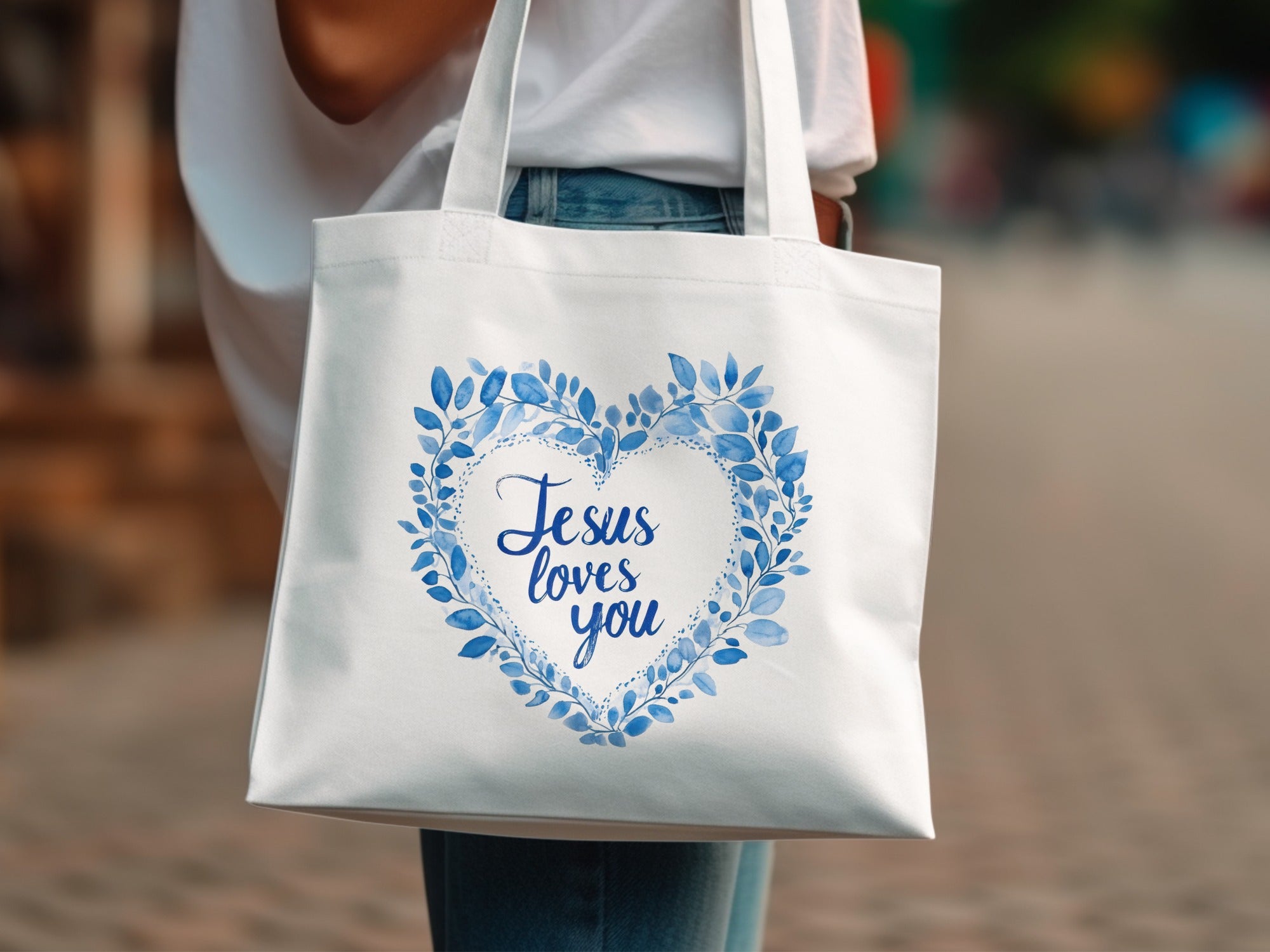 White tote bag with a blue leafy heart and "Jesus loves you" text.