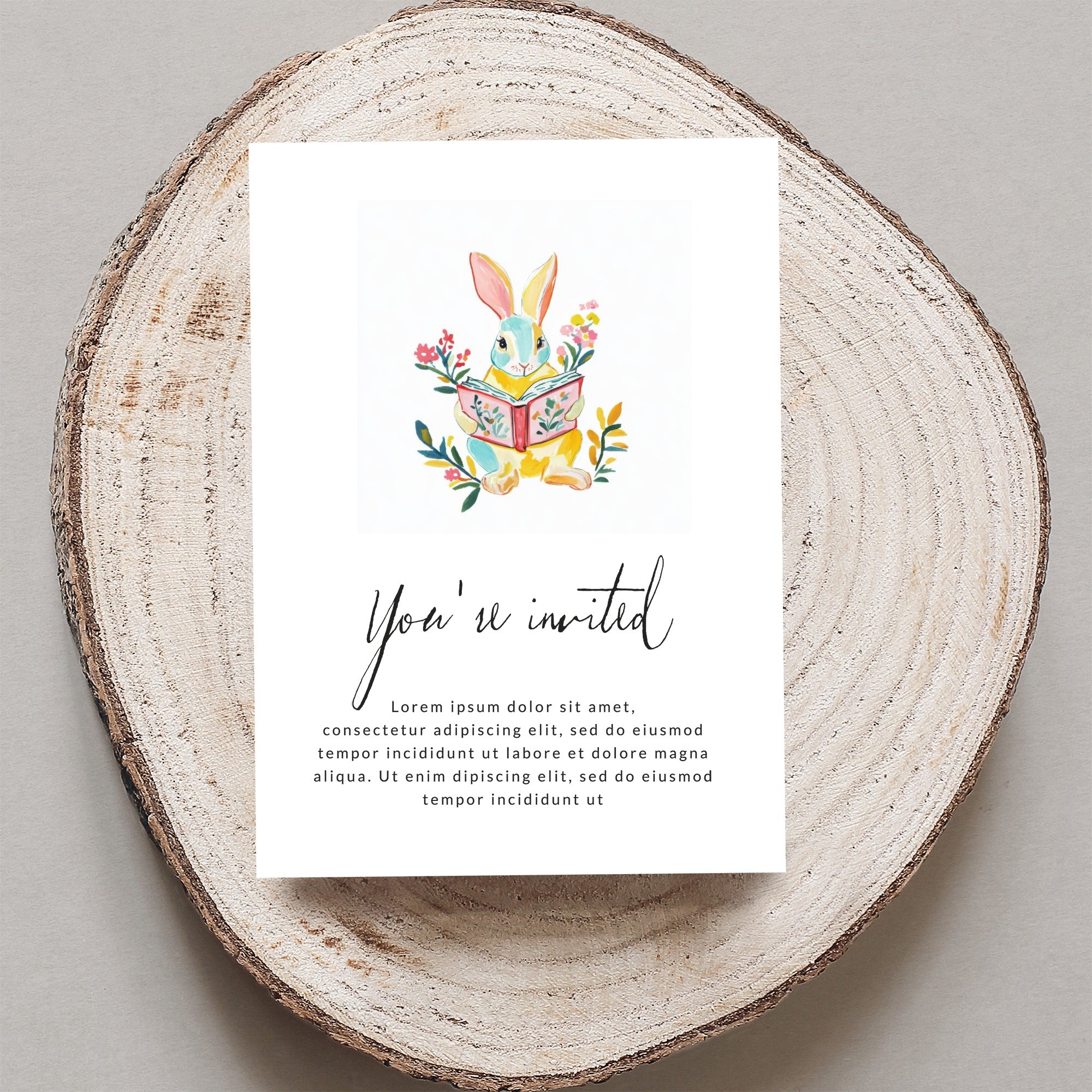Illustrated bunny reading book on a card with "You're invited" text.