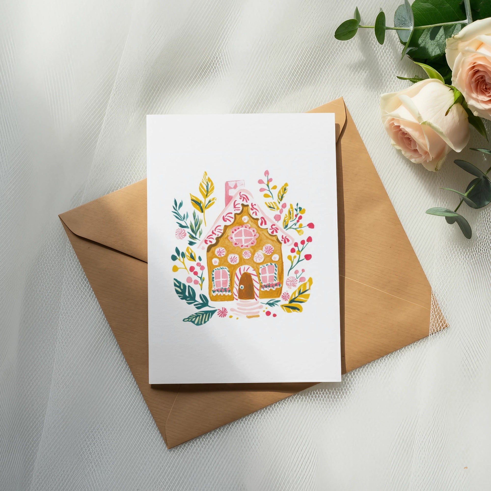 Gingerbread house card on envelope with roses and eucalyptus.