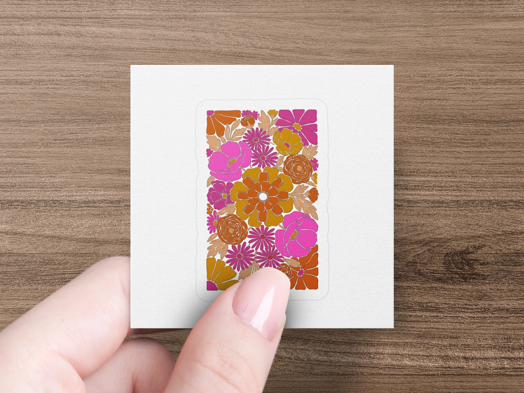 Hand holding a square sticker with a retro floral pattern in orange and pink.