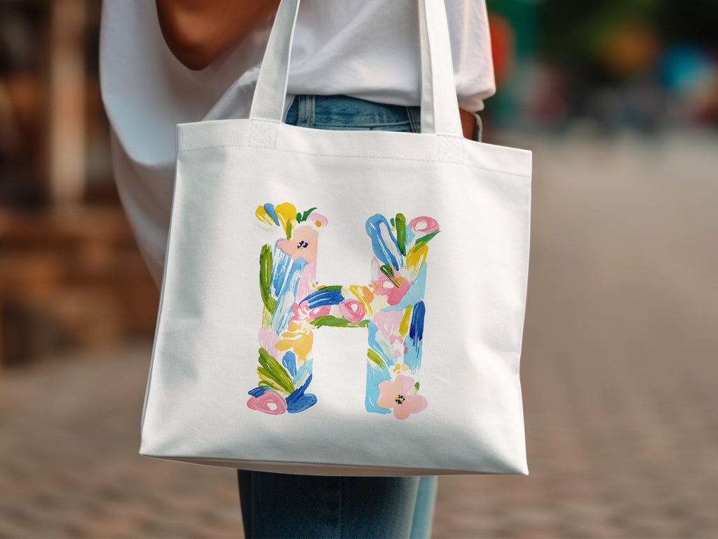 White tote bag with a large, colorful floral letter H design.