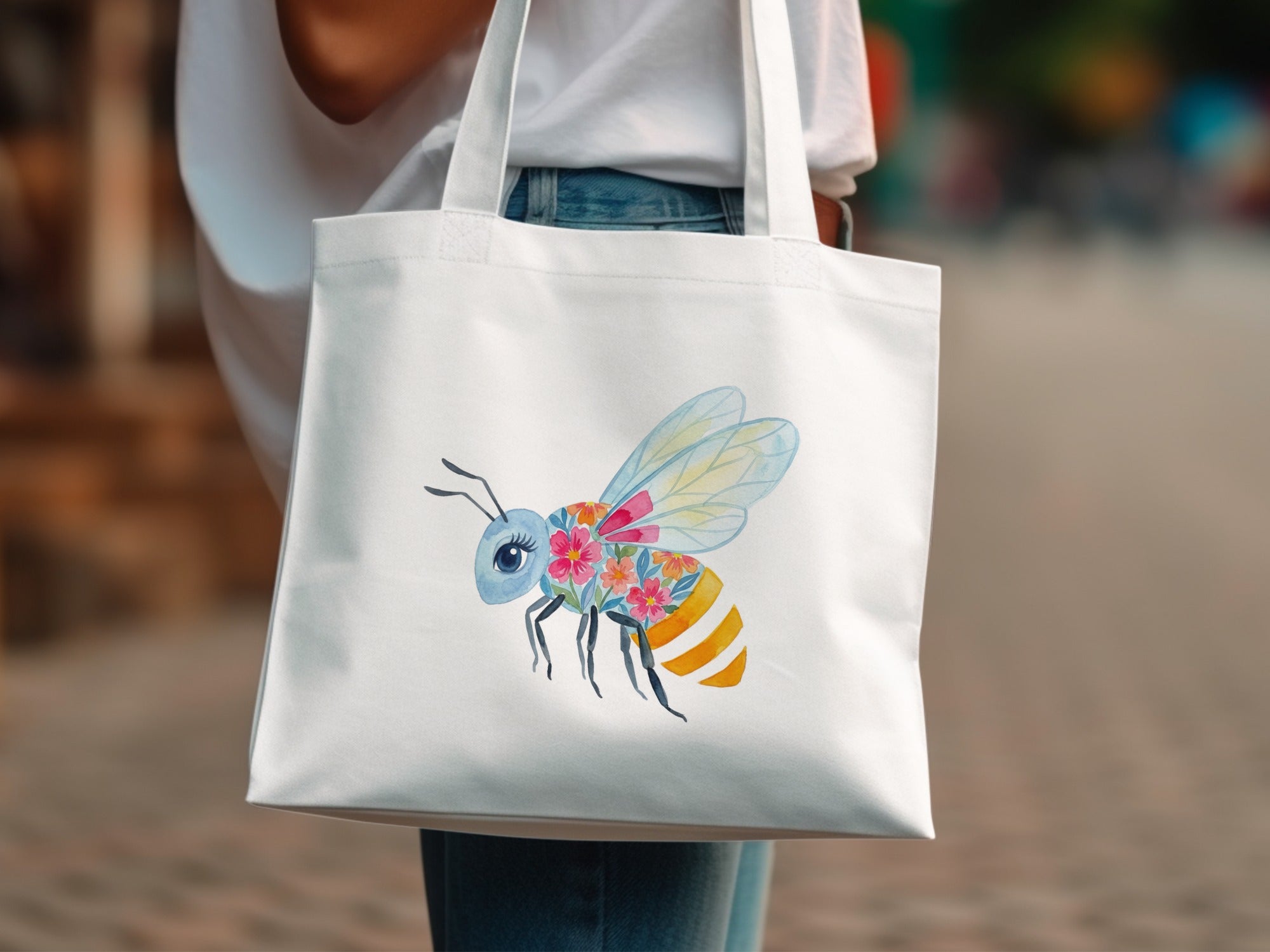 White tote bag with a watercolor bee illustration featuring floral wings and striped body.