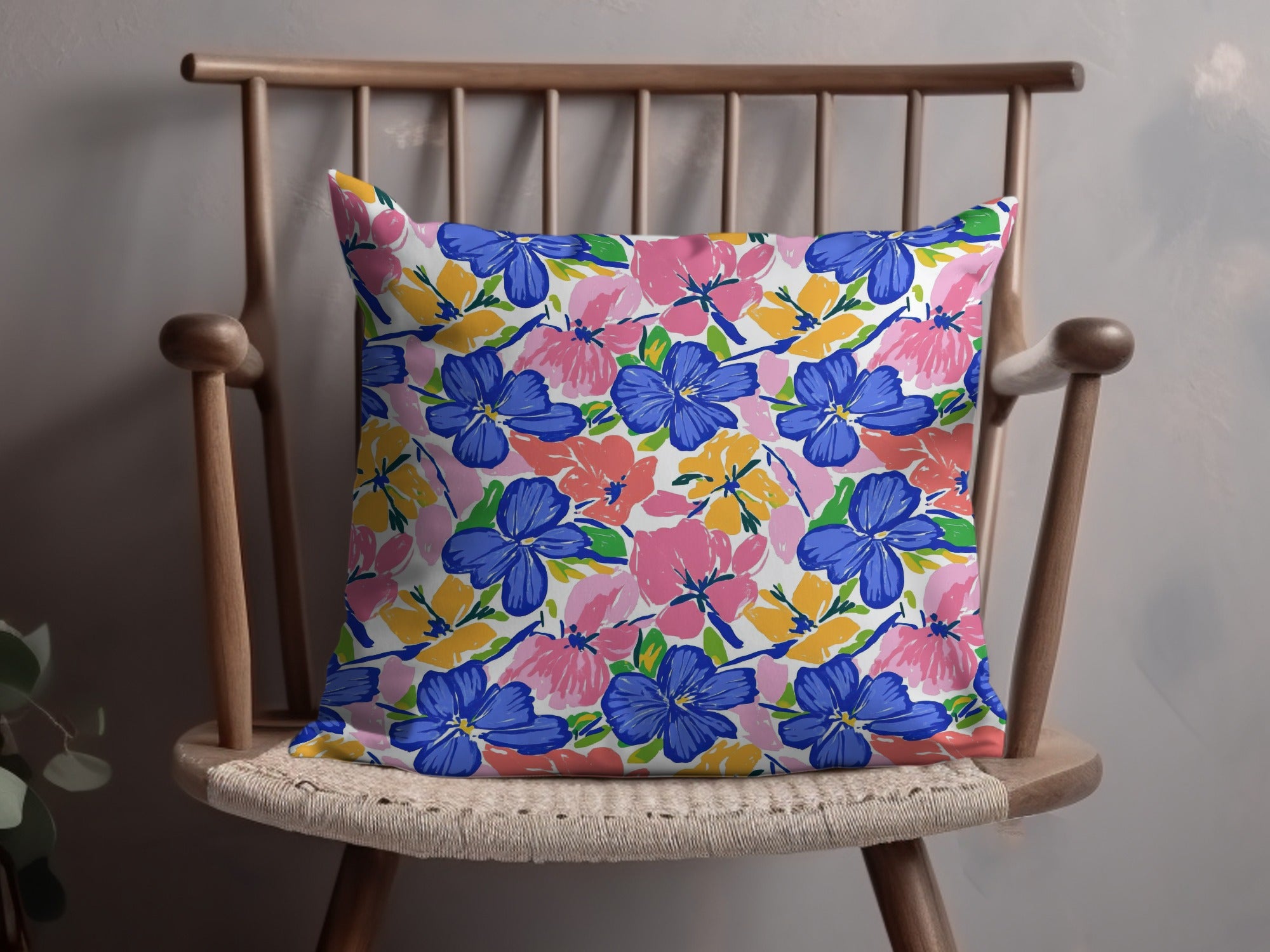 Floral throw pillow with blue, pink, and yellow flowers on a wooden chair.