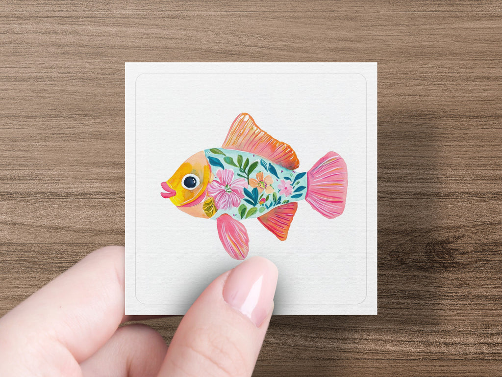 Pink fish with colorful floral patterns on white card held by fingers.