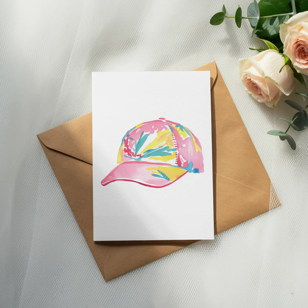 Pink baseball cap with colorful abstract pattern on white card over brown envelope.