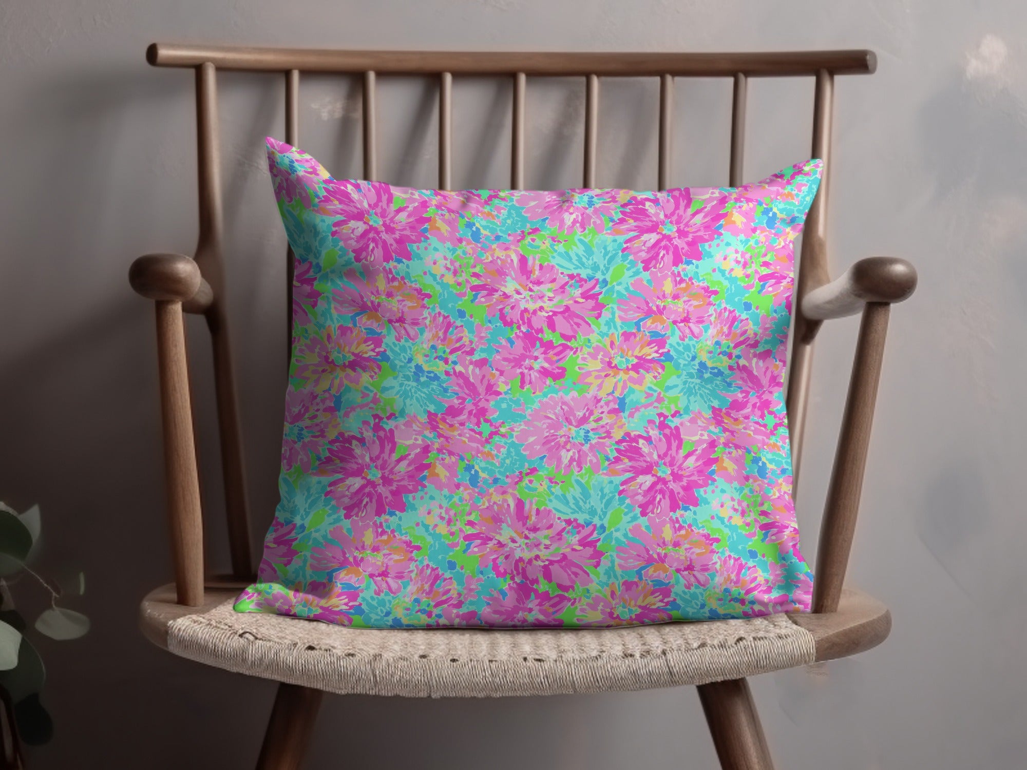 Bright floral pattern pillow with pink, blue, and green flowers on a wooden chair.
