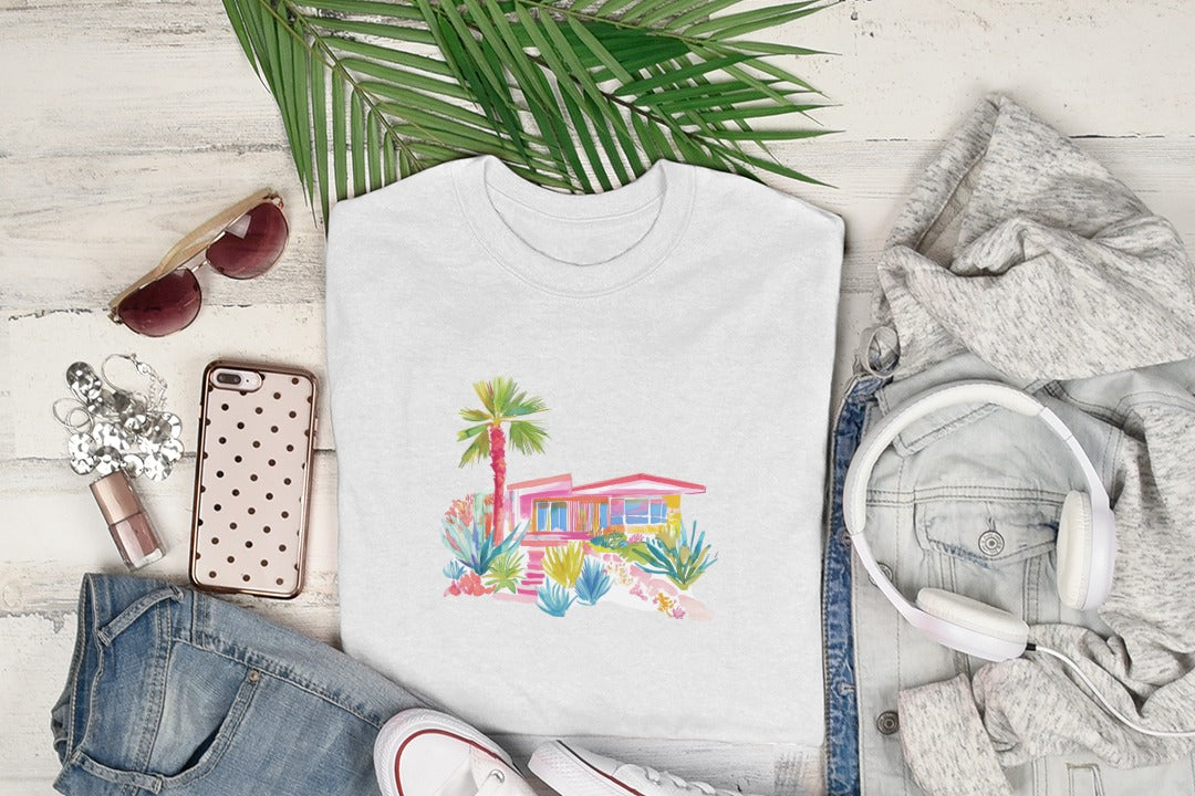 White t-shirt with a colorful watercolor drawing of a mid-century modern house and palm tree.