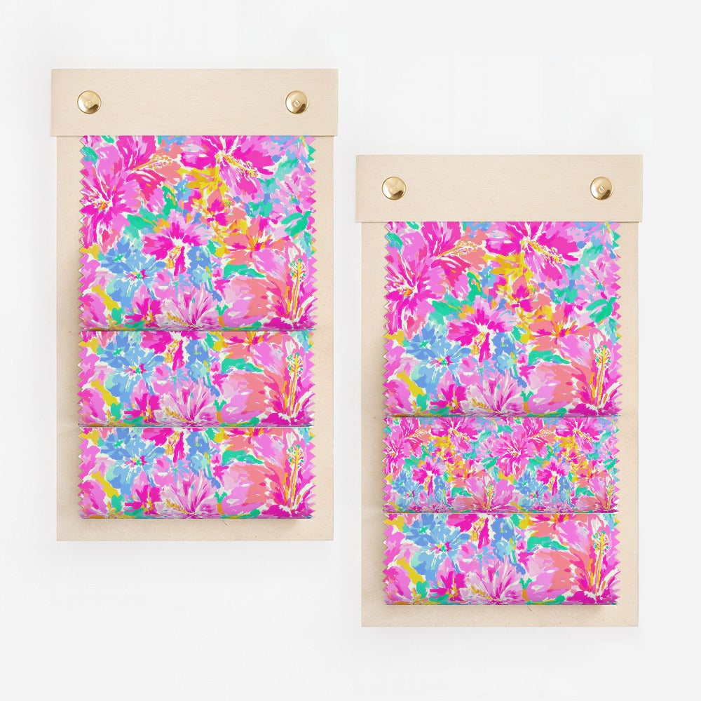 Two fabric swatches with a vibrant floral pattern on a light wooden backing.