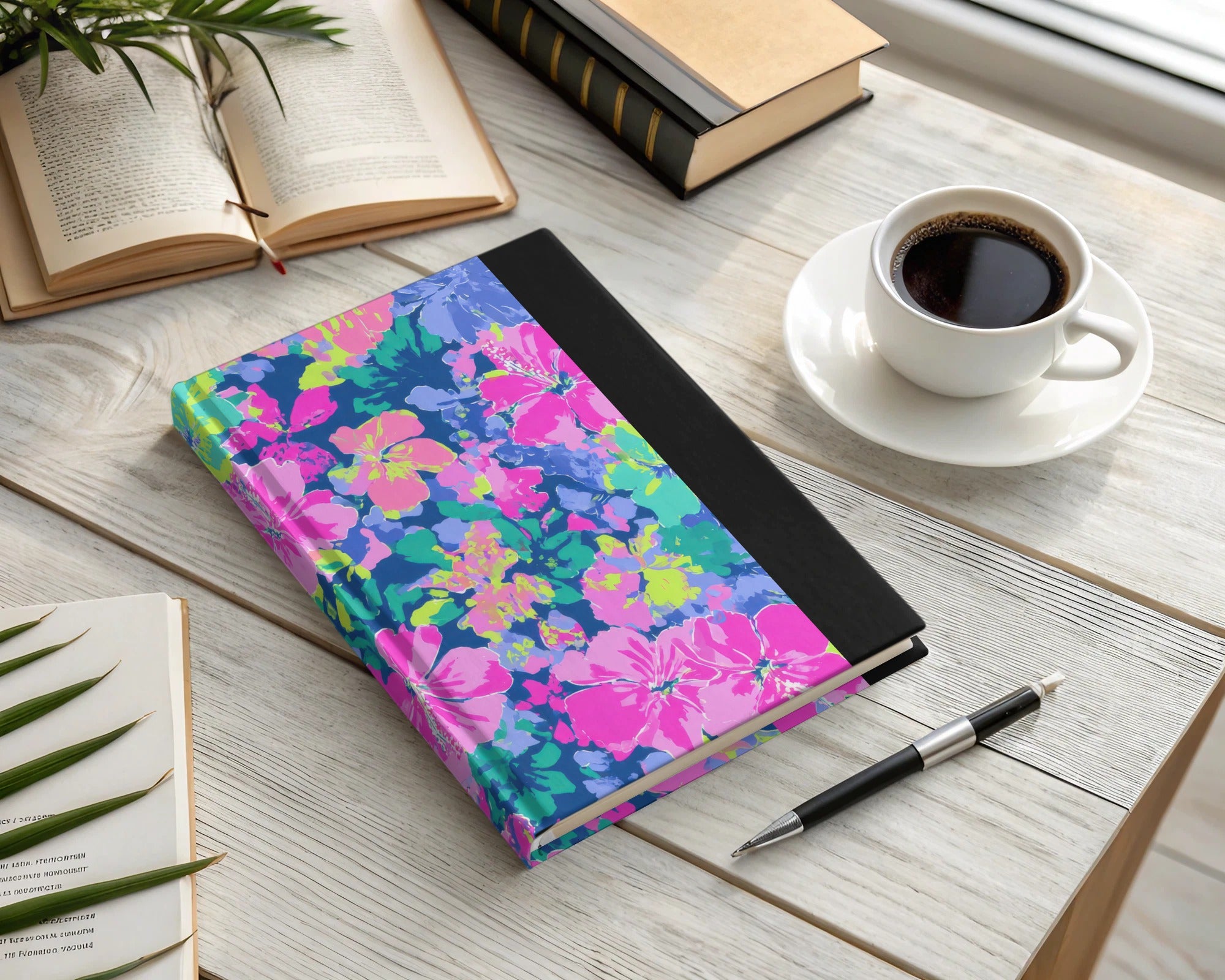 Floral patterned notebook with black spine and coffee cup on desk.