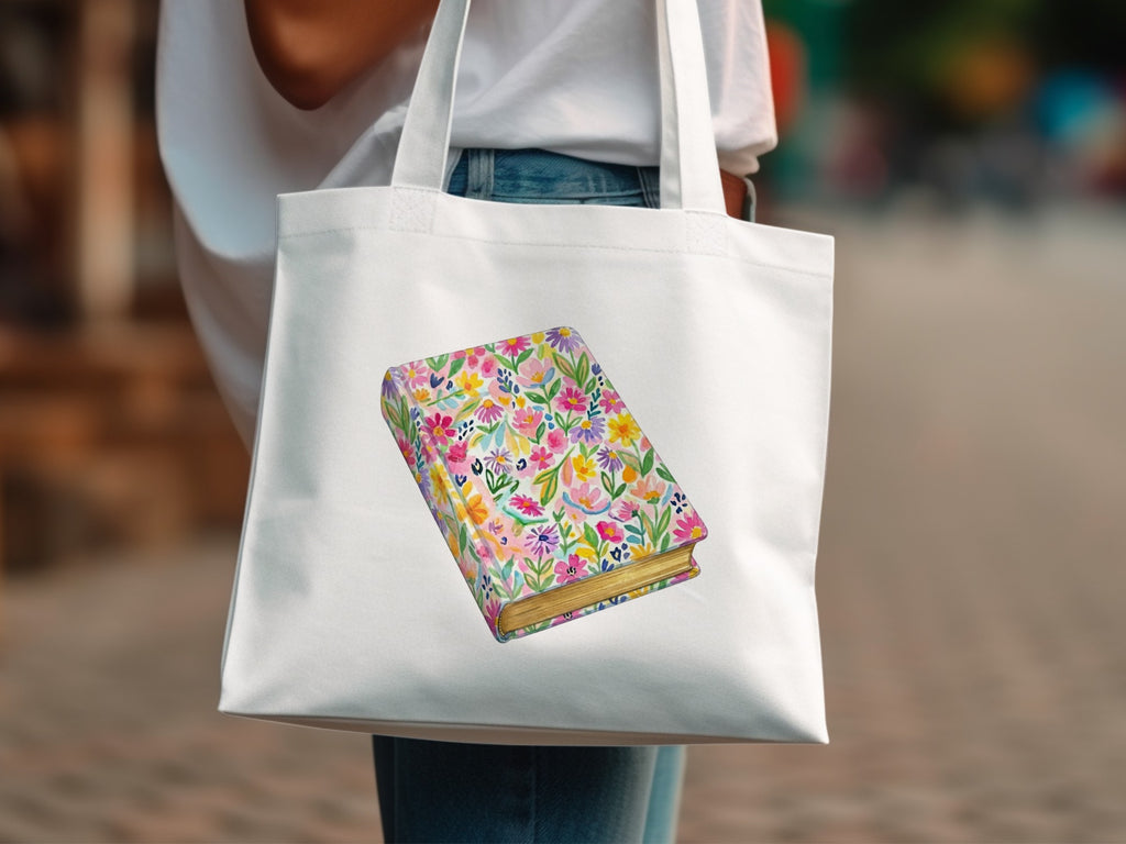 White tote bag with a colorful floral patterned book design.