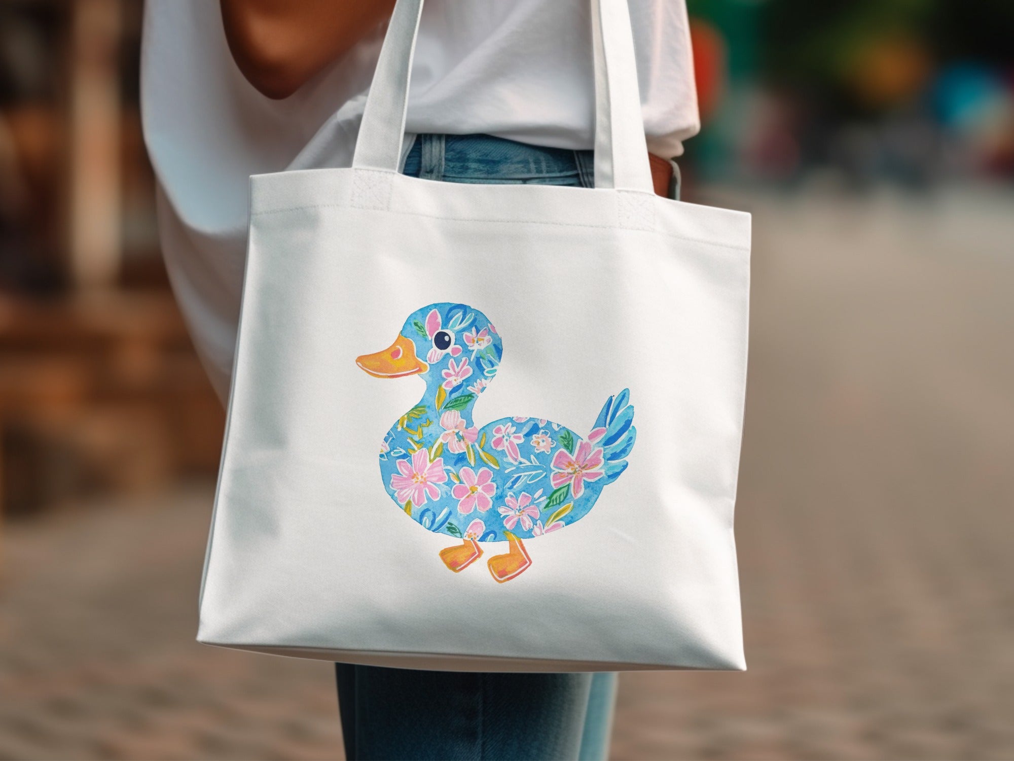 White tote bag with a cheerful blue duckling illustration adorned with pink flowers.