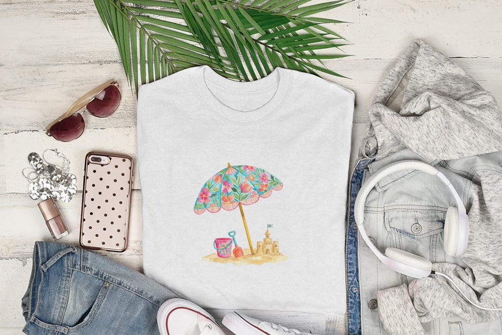 White t-shirt featuring a watercolor beach umbrella, pail, and sandcastle design.