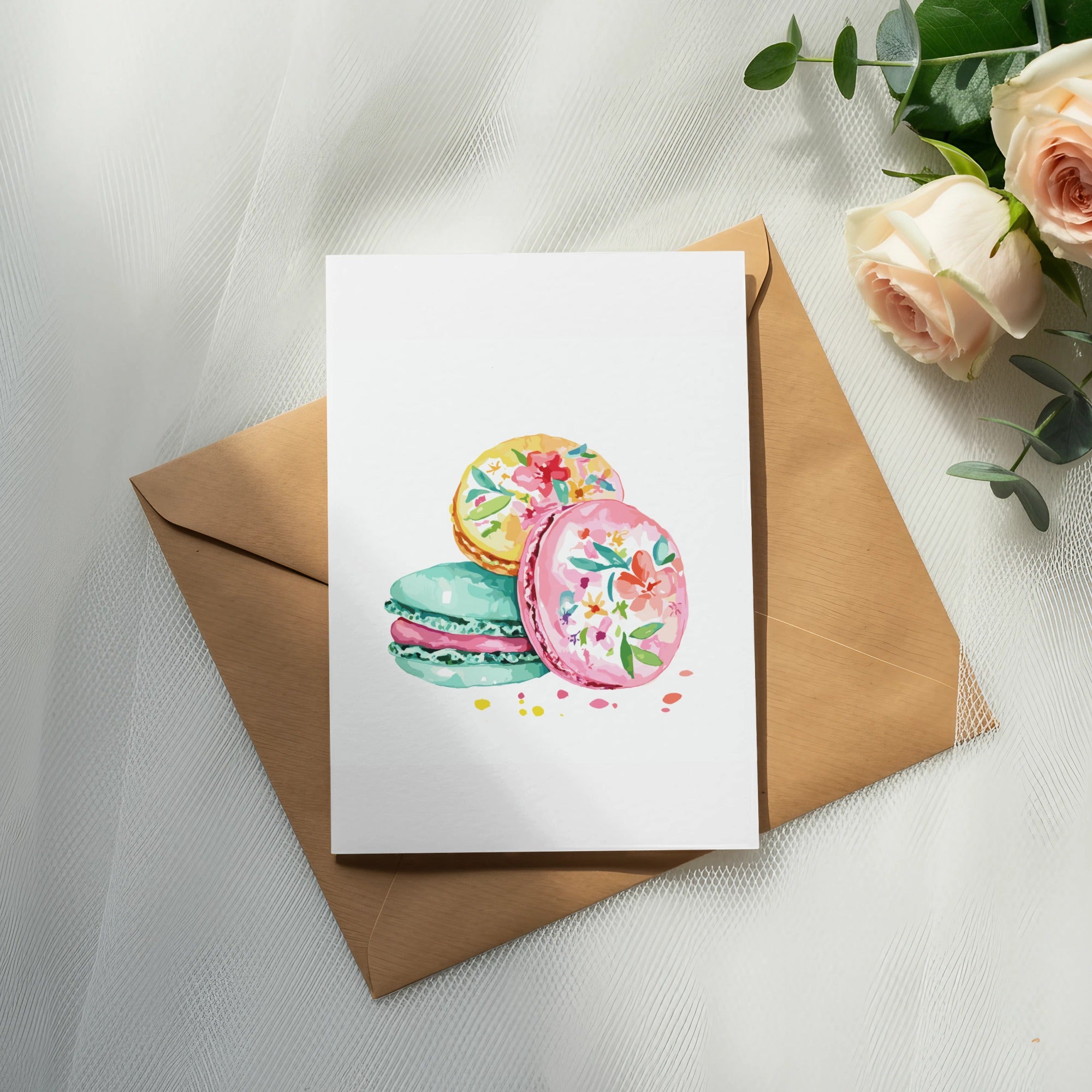 Watercolor macarons with floral designs on a card over an envelope.