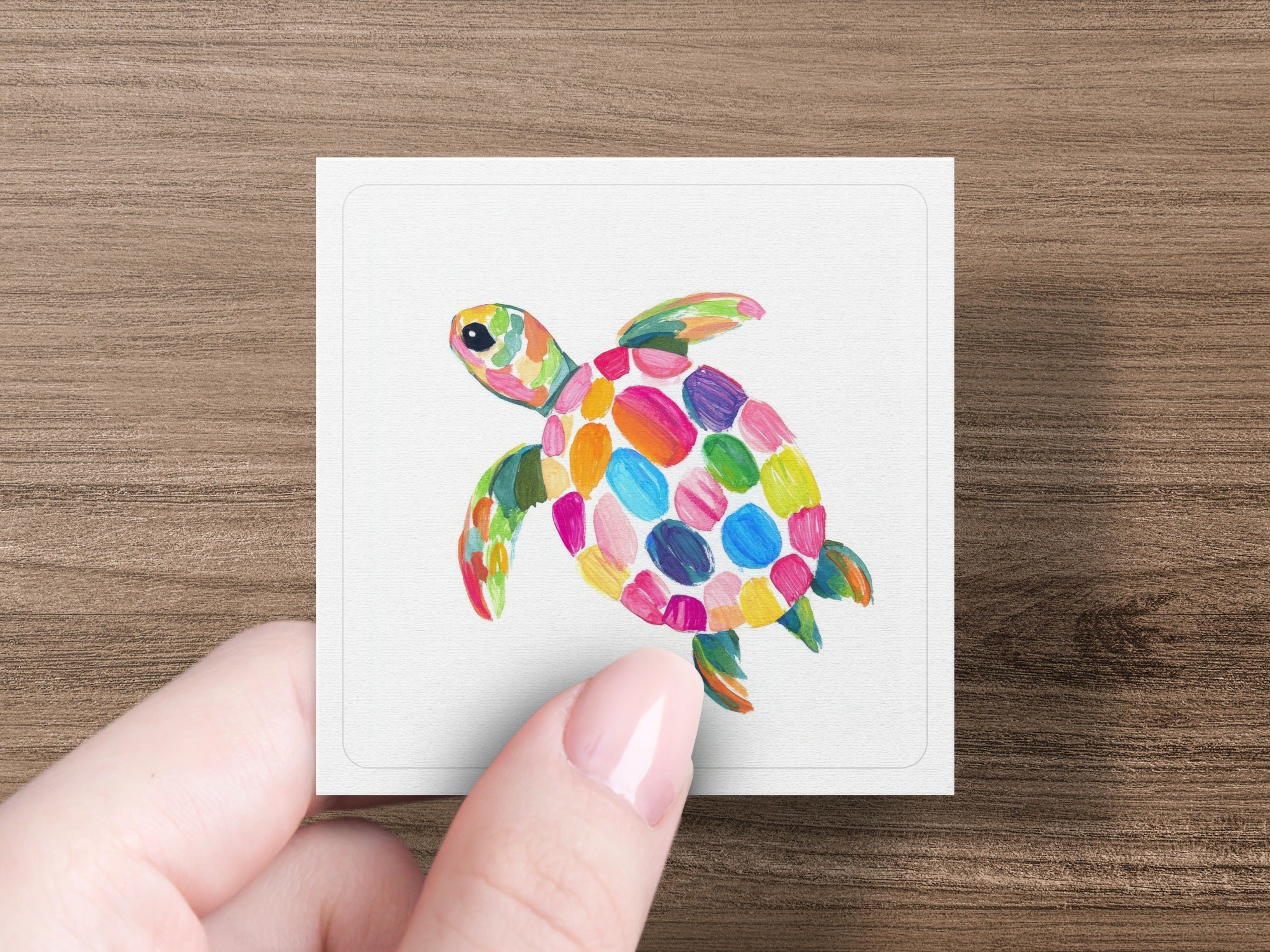 Colorful painted sea turtle on a white card held by a hand.