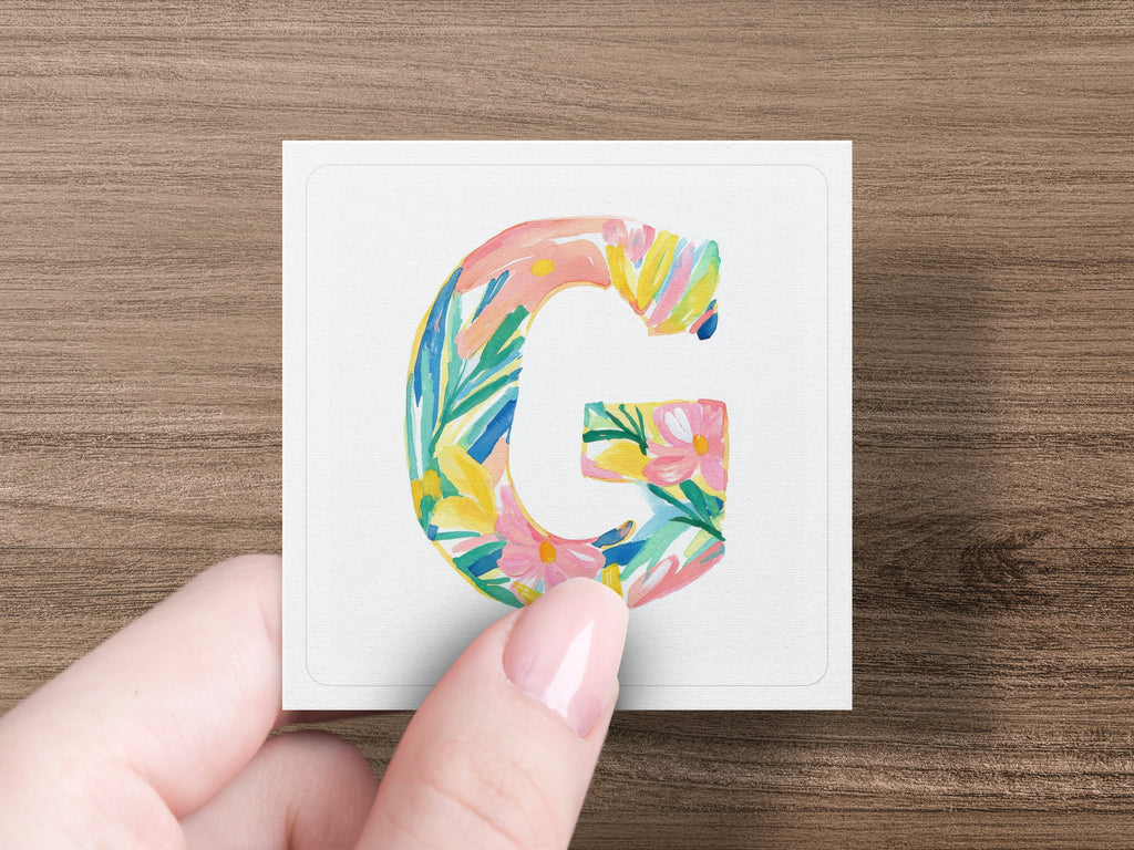 Floral letter G on card held by a hand.