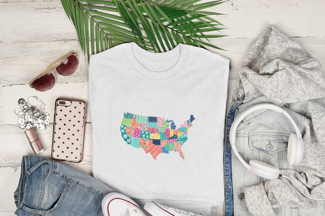 White t-shirt with colorful patchwork USA map graphic, styled with jeans and headphones.