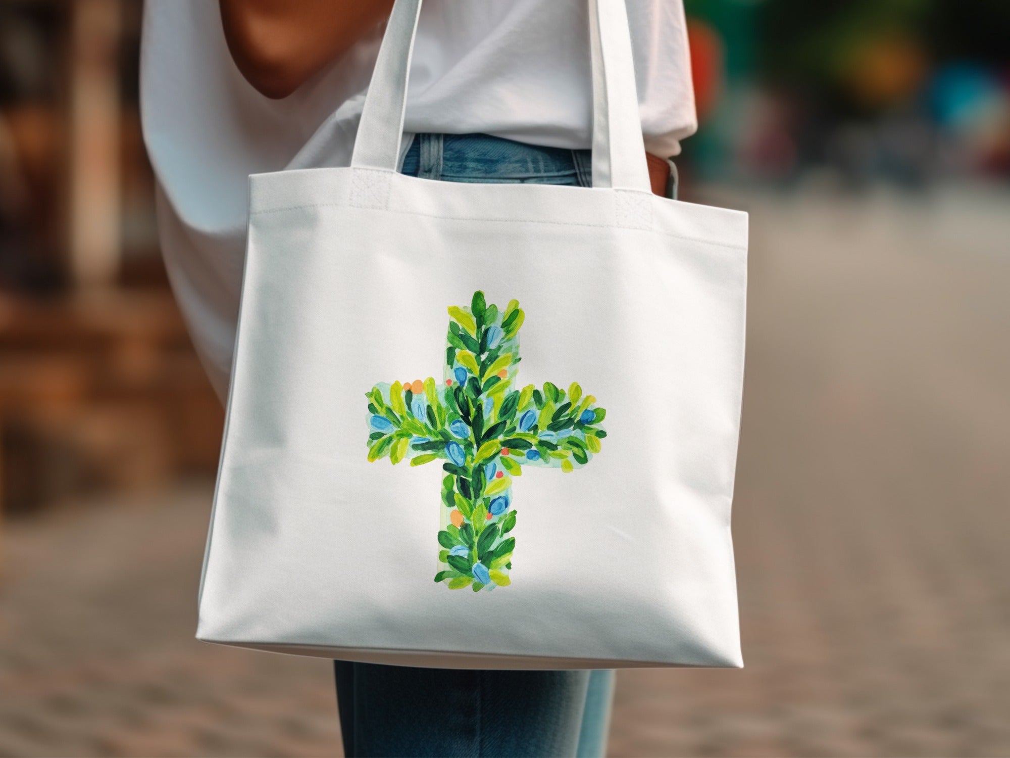 White canvas tote bag with a green and blue floral cross design.