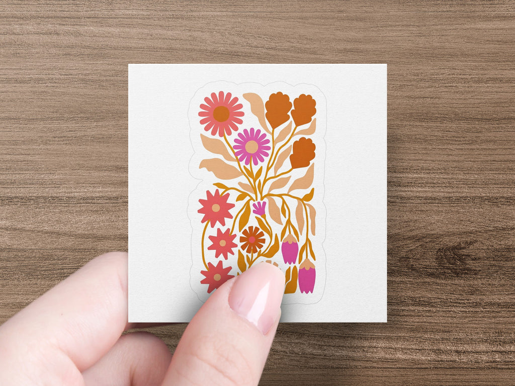 Hand holding sticker with folk art floral design in pinks and oranges.