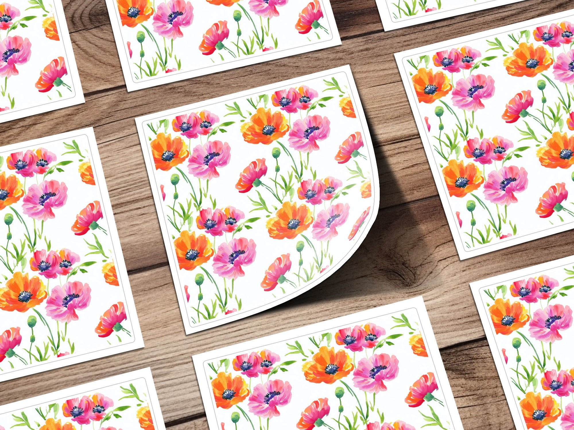 Watercolor poppy flower pattern on white cards with curled edges on a wooden background.