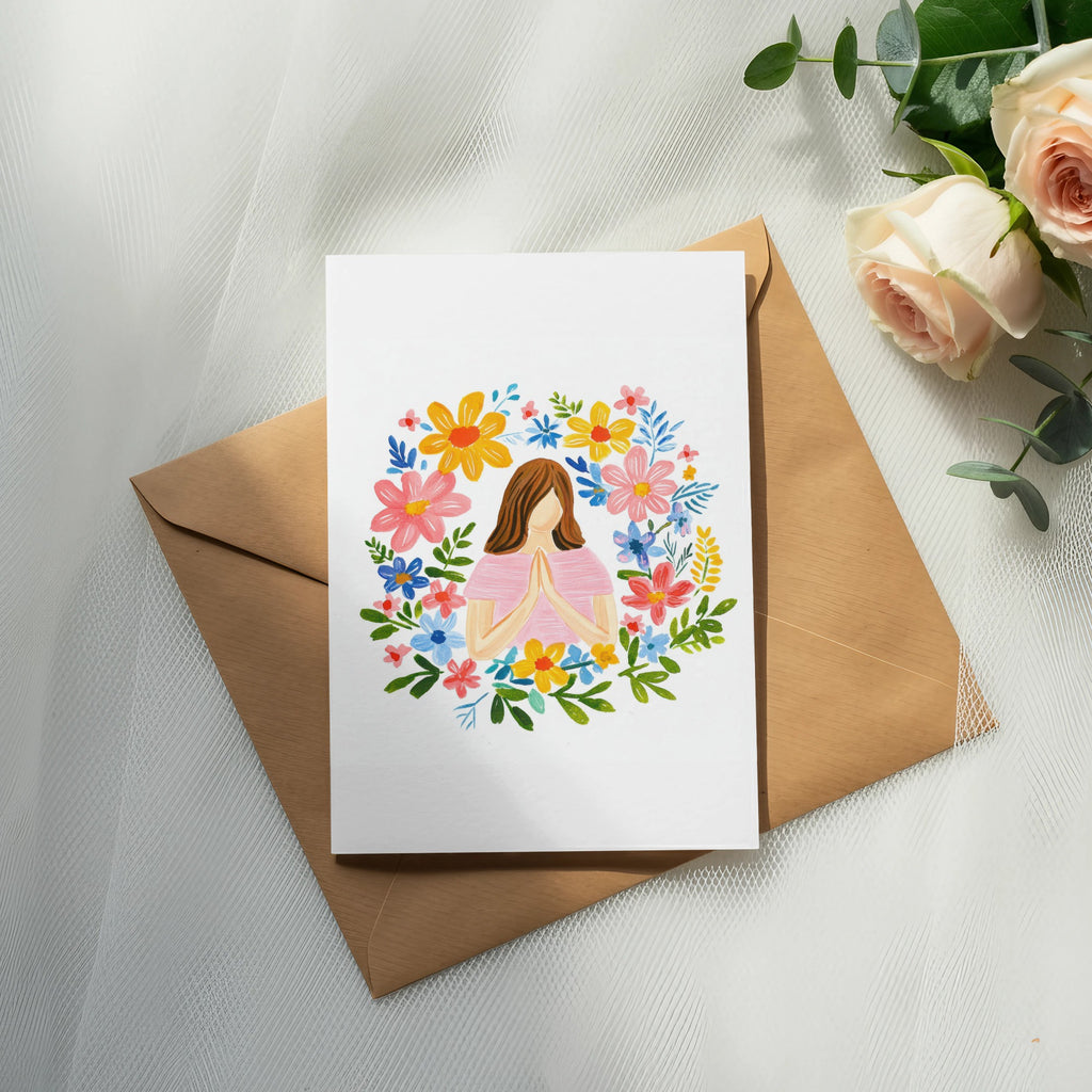 Greeting card with floral wreath and praying hands, on a brown envelope.
