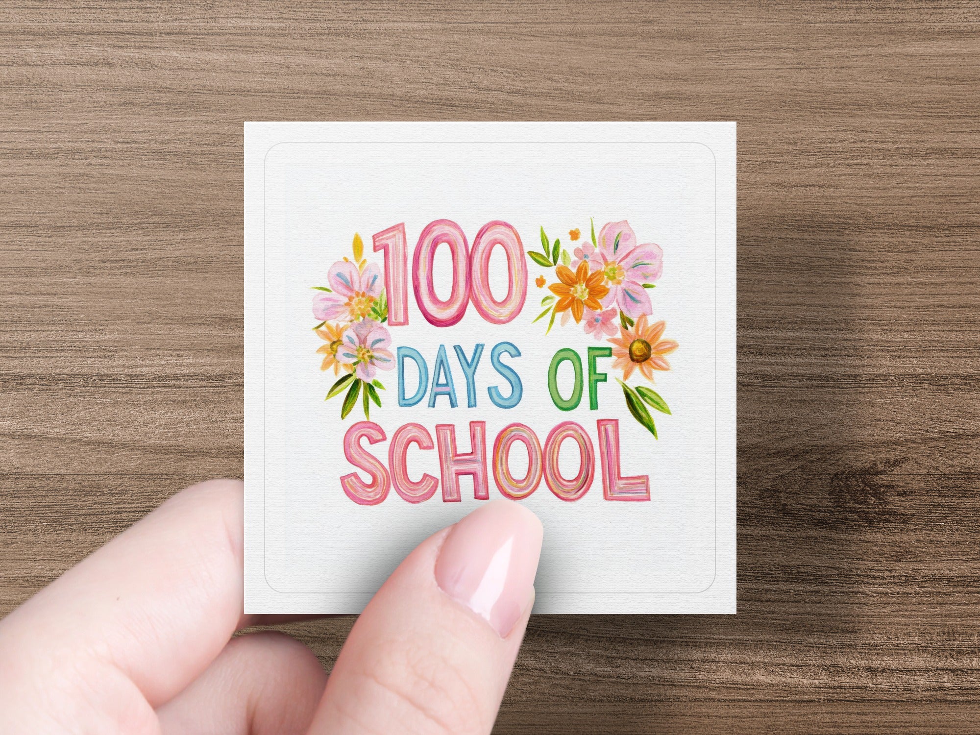 Card with "100 DAYS OF SCHOOL" text and floral decorations, held by a hand.