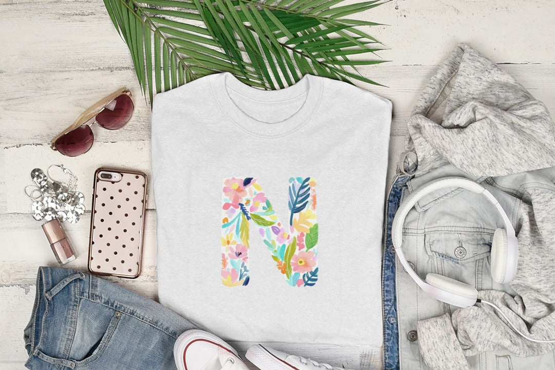 White t-shirt with colorful floral letter "N" design, viewed from above.