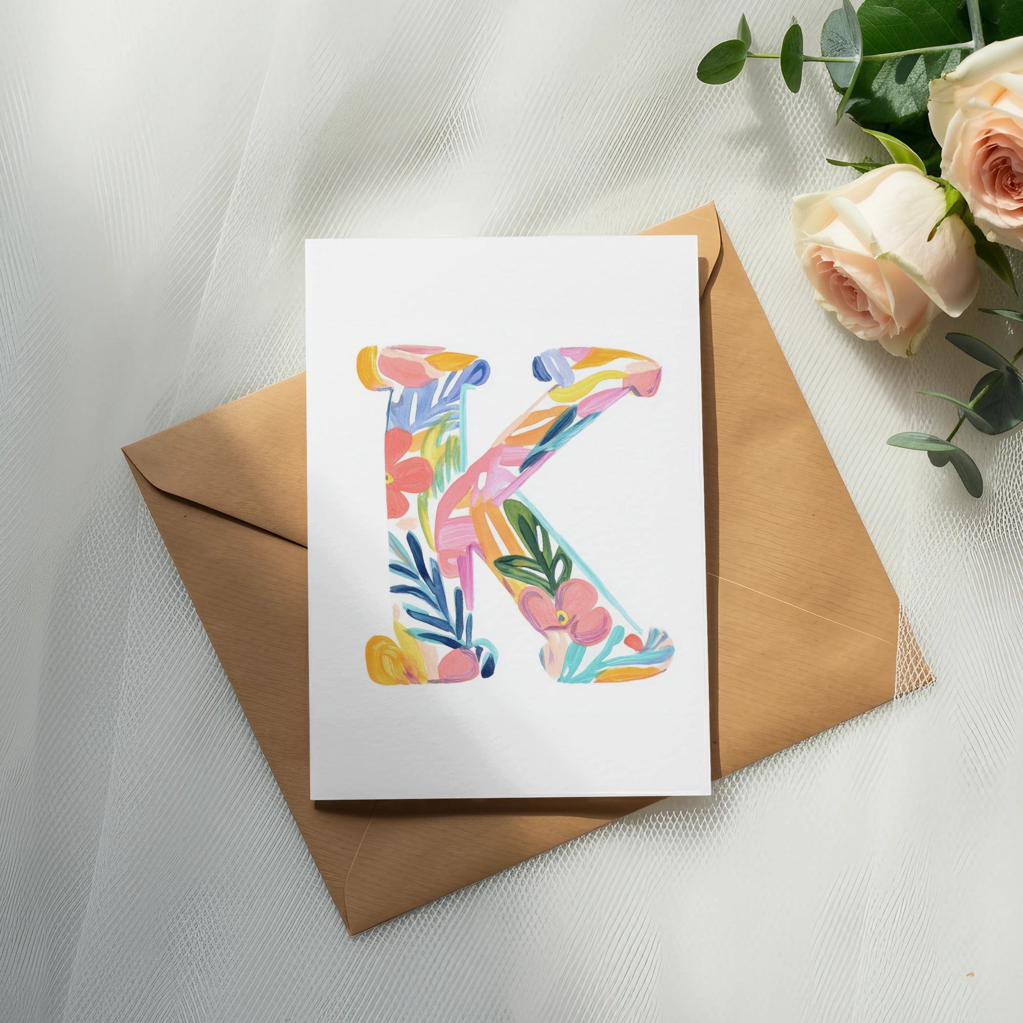 Floral letter K on a card atop a kraft envelope with roses.