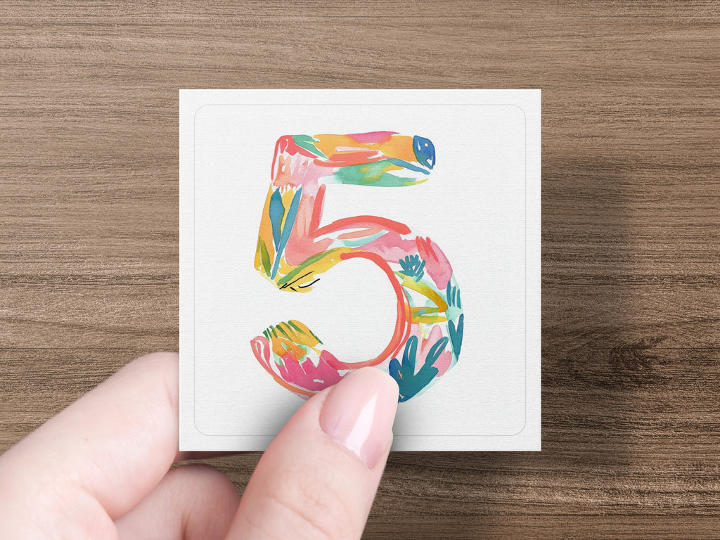 Hand holding a square card with a colorful, abstract number 5 design.