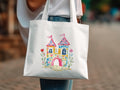 White tote bag with watercolor illustration of a colorful castle with pink flags.