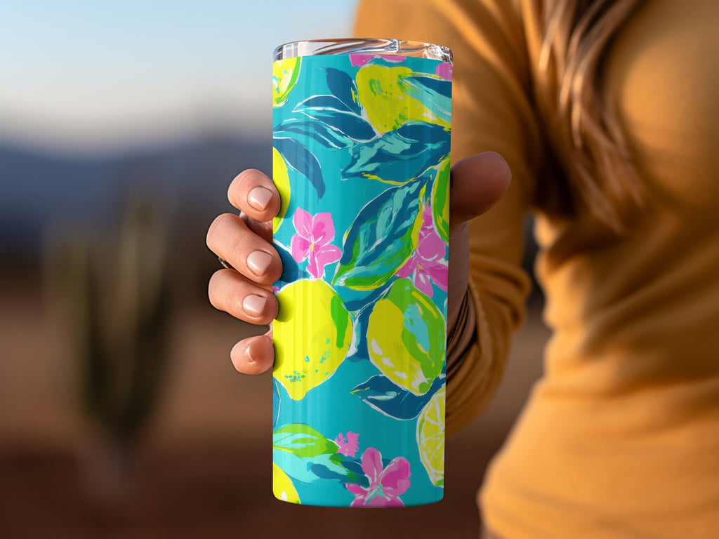 Teal tumbler with a colorful lemon and floral pattern, held by a person.