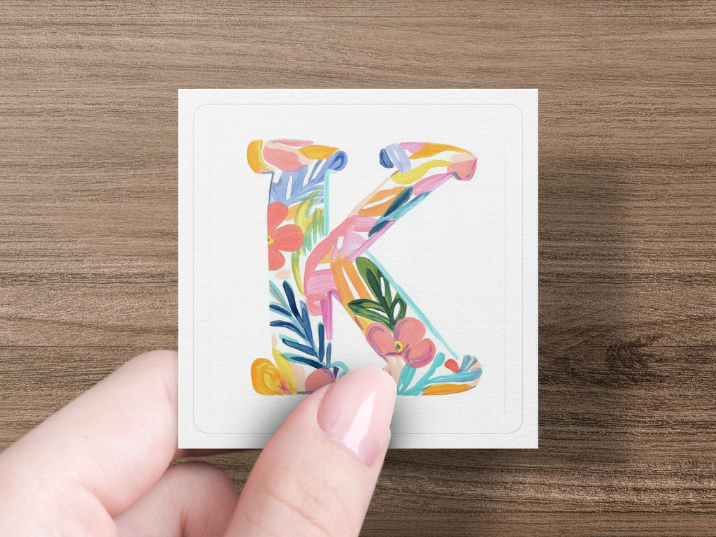 Floral letter K on white card held by a hand.