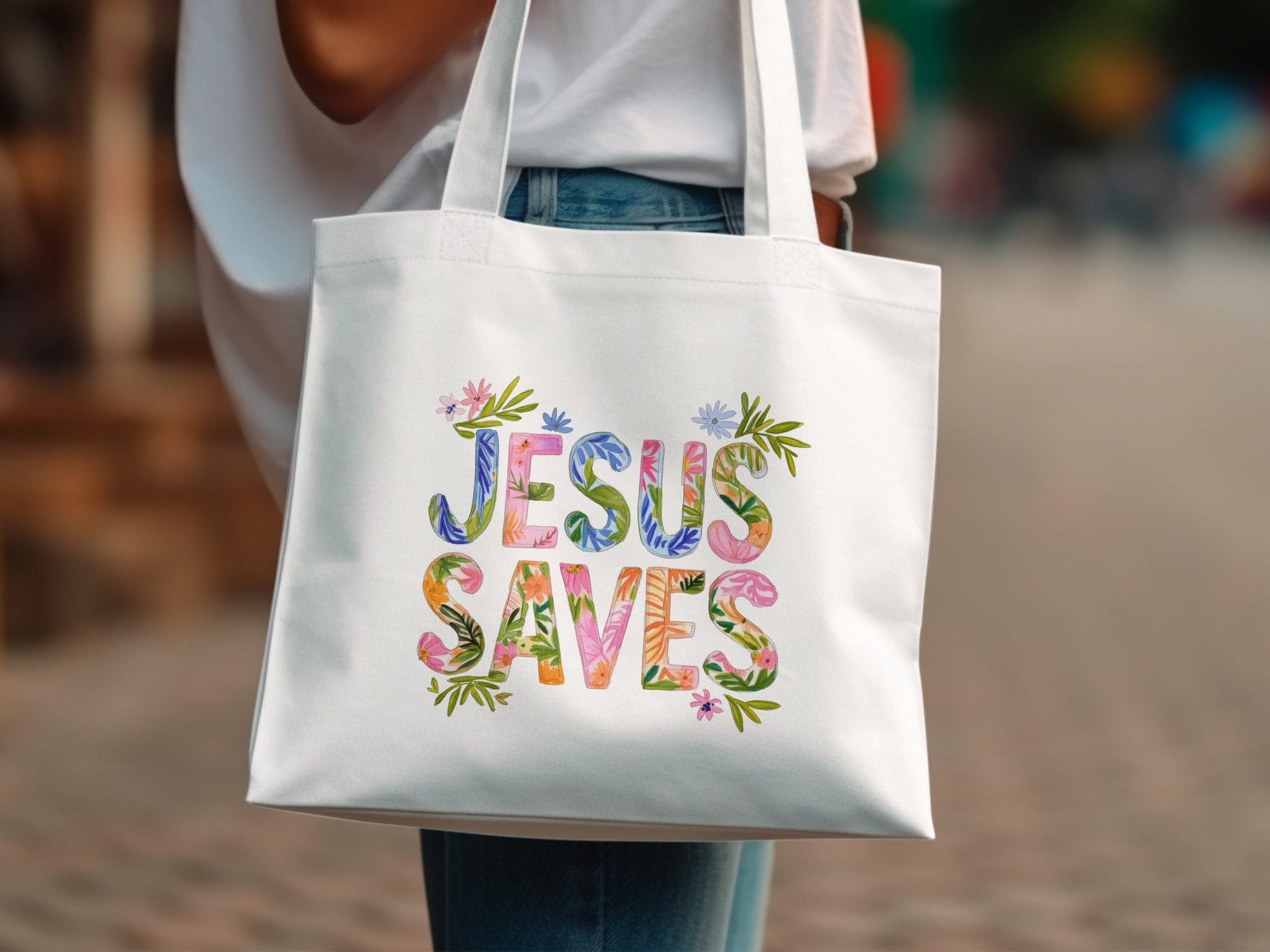 White tote bag with colorful "Jesus Saves" text and floral accents.