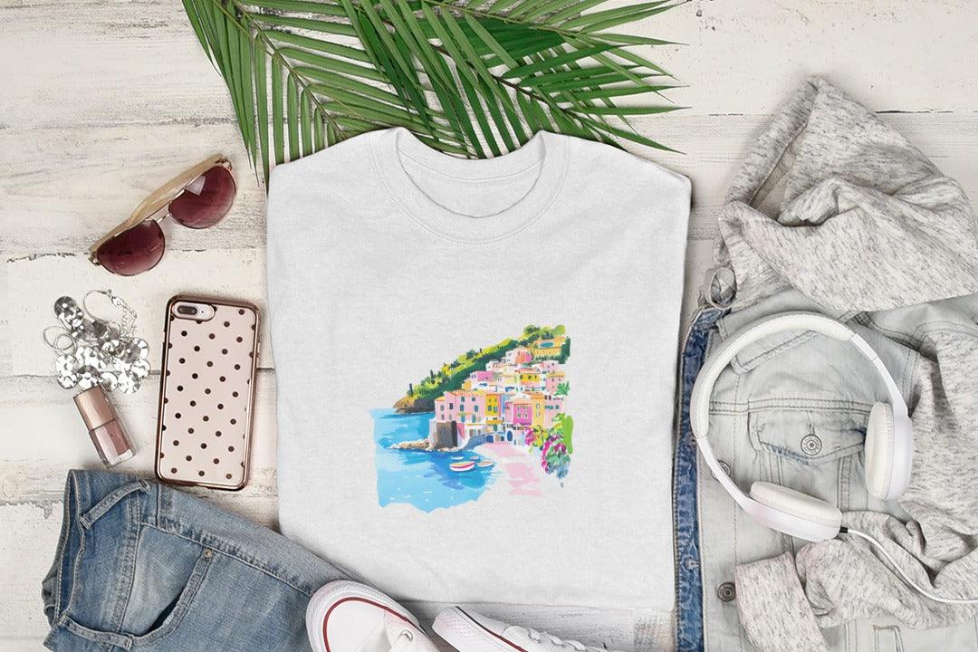 White t-shirt with colorful coastal town graphic, styled with denim and headphones.