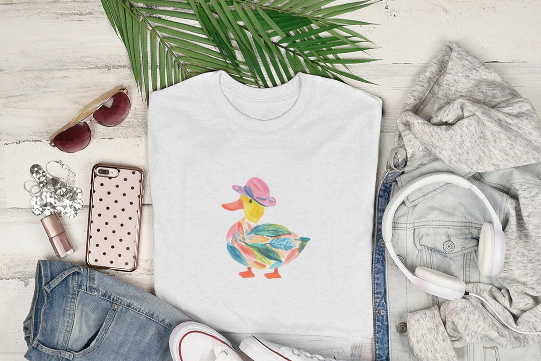 White t-shirt with a watercolor duck wearing a pink hat and colorful leaf pattern.