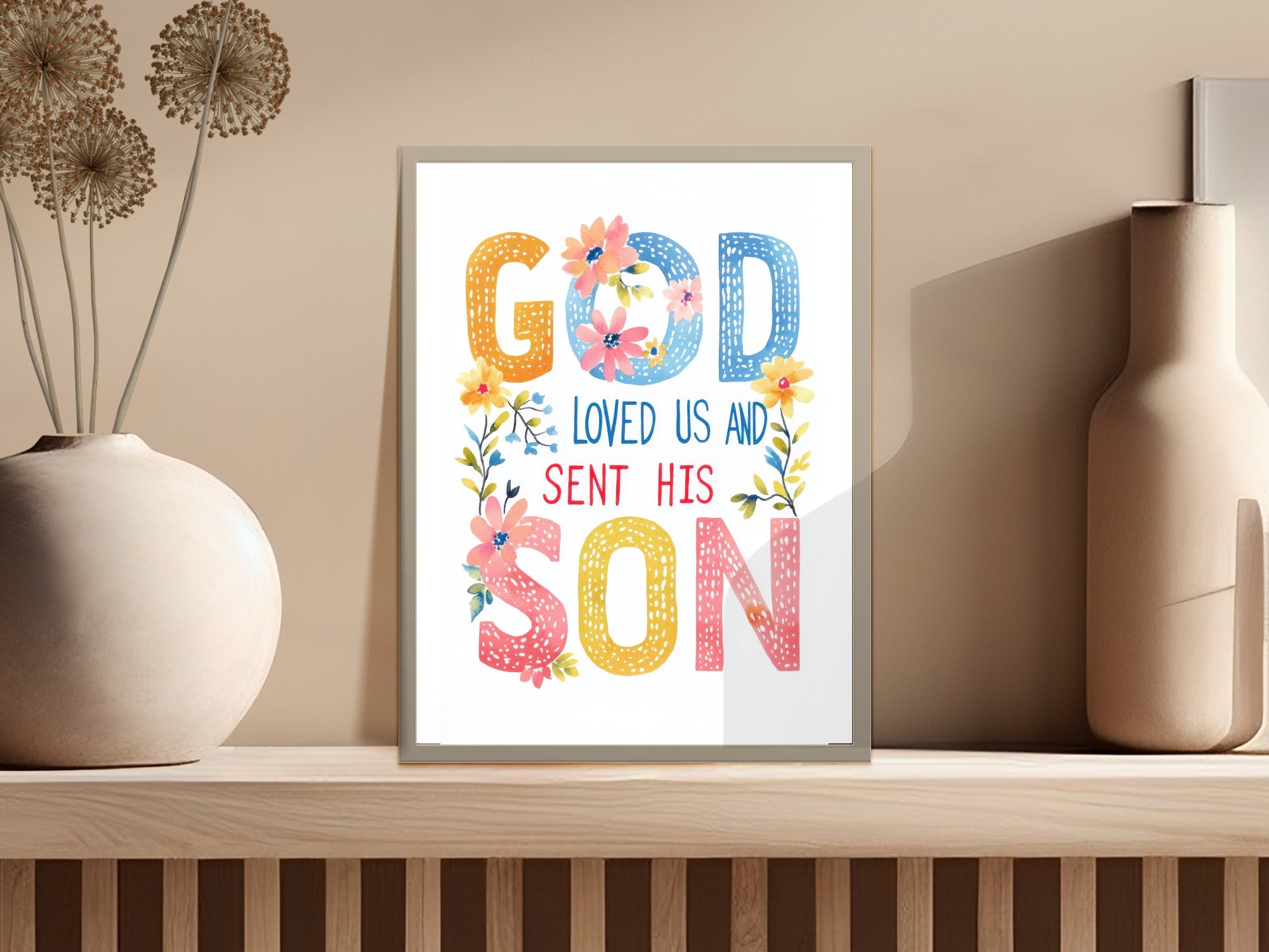 Framed artwork with colorful text that reads "God Loved Us And Sent His Son."