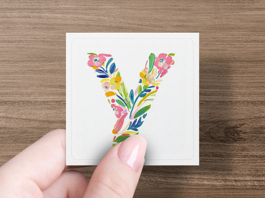 Hand holding a square card with a colorful floral letter "Y" design.