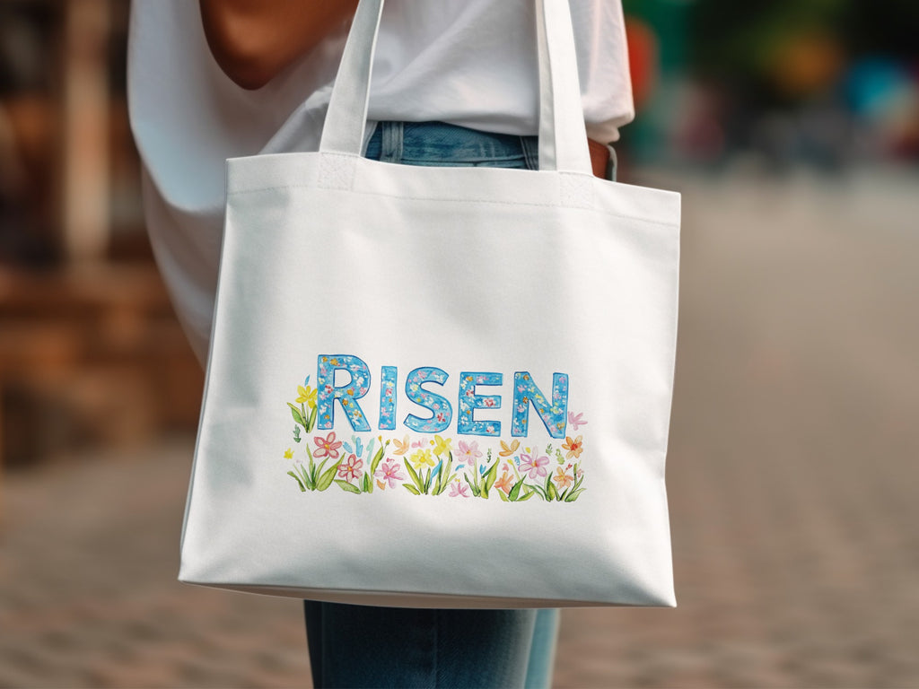 White canvas tote bag with "RISEN" text surrounded by colorful floral illustrations.
