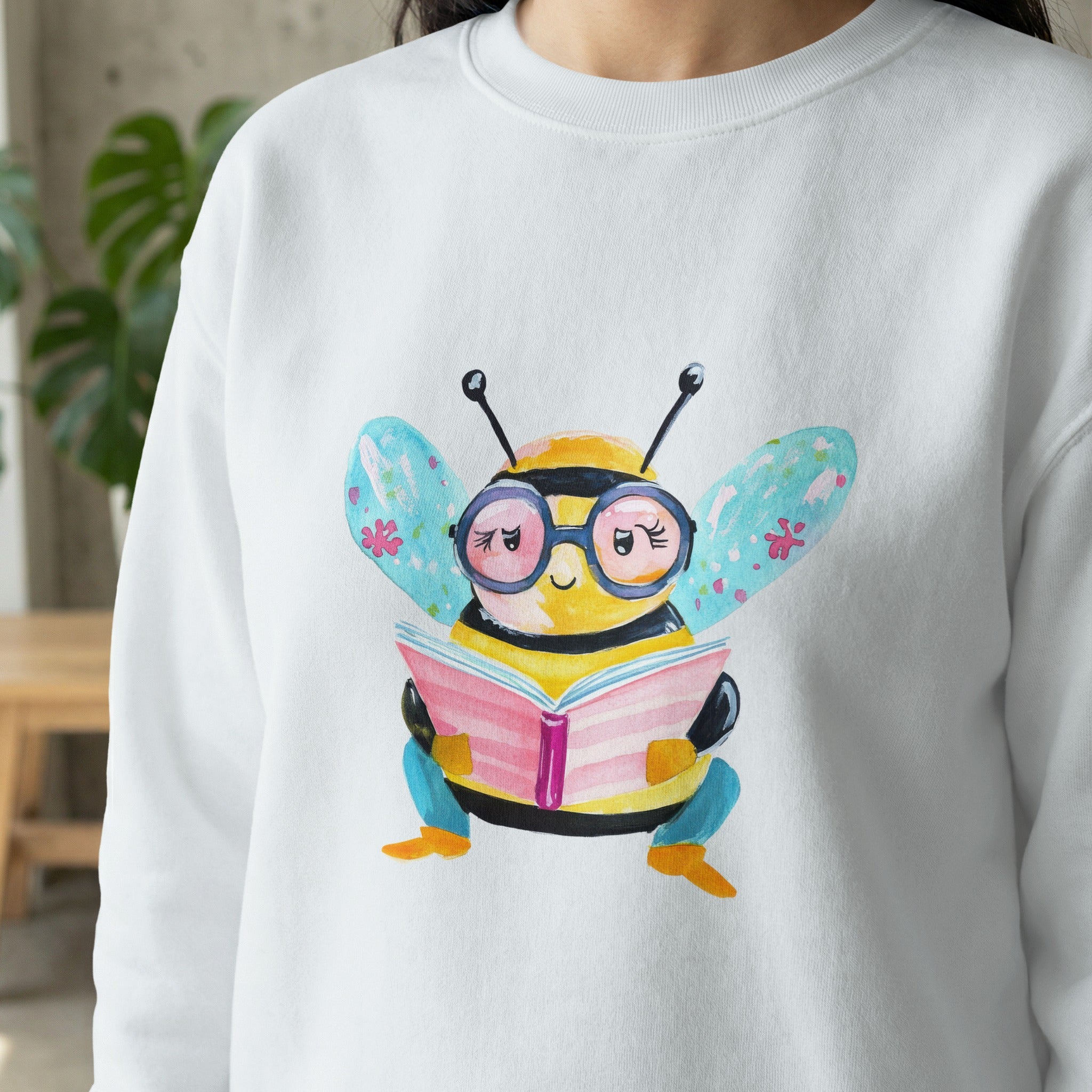 Whimsical bee wearing glasses reads a book, printed on a white sweatshirt.