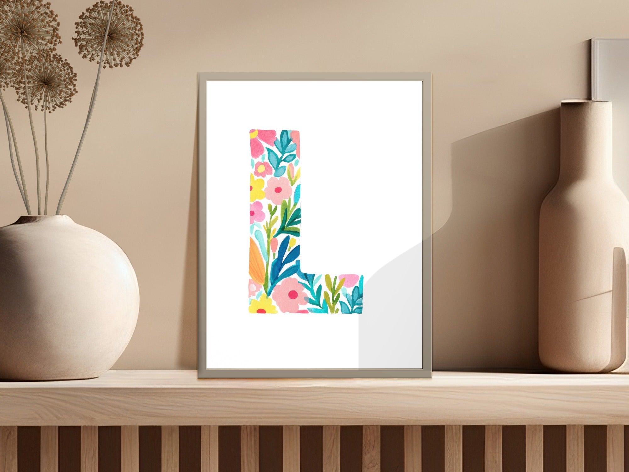 Floral letter L artwork in a white frame on a shelf.