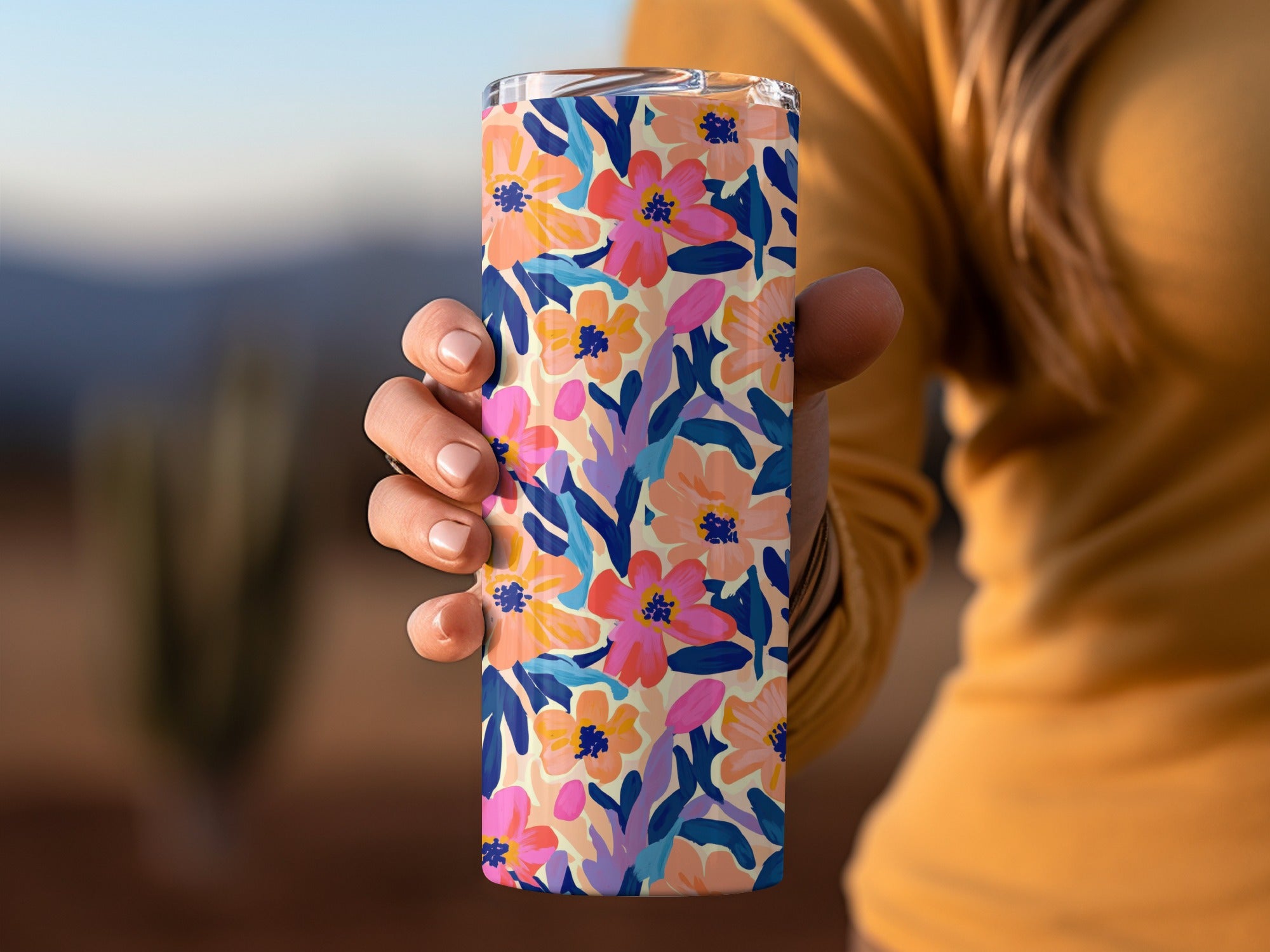 Floral pattern tumbler held by hand against a blurred outdoor background.