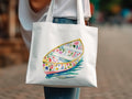 White canvas tote bag with watercolor painting of a floral boat on water.