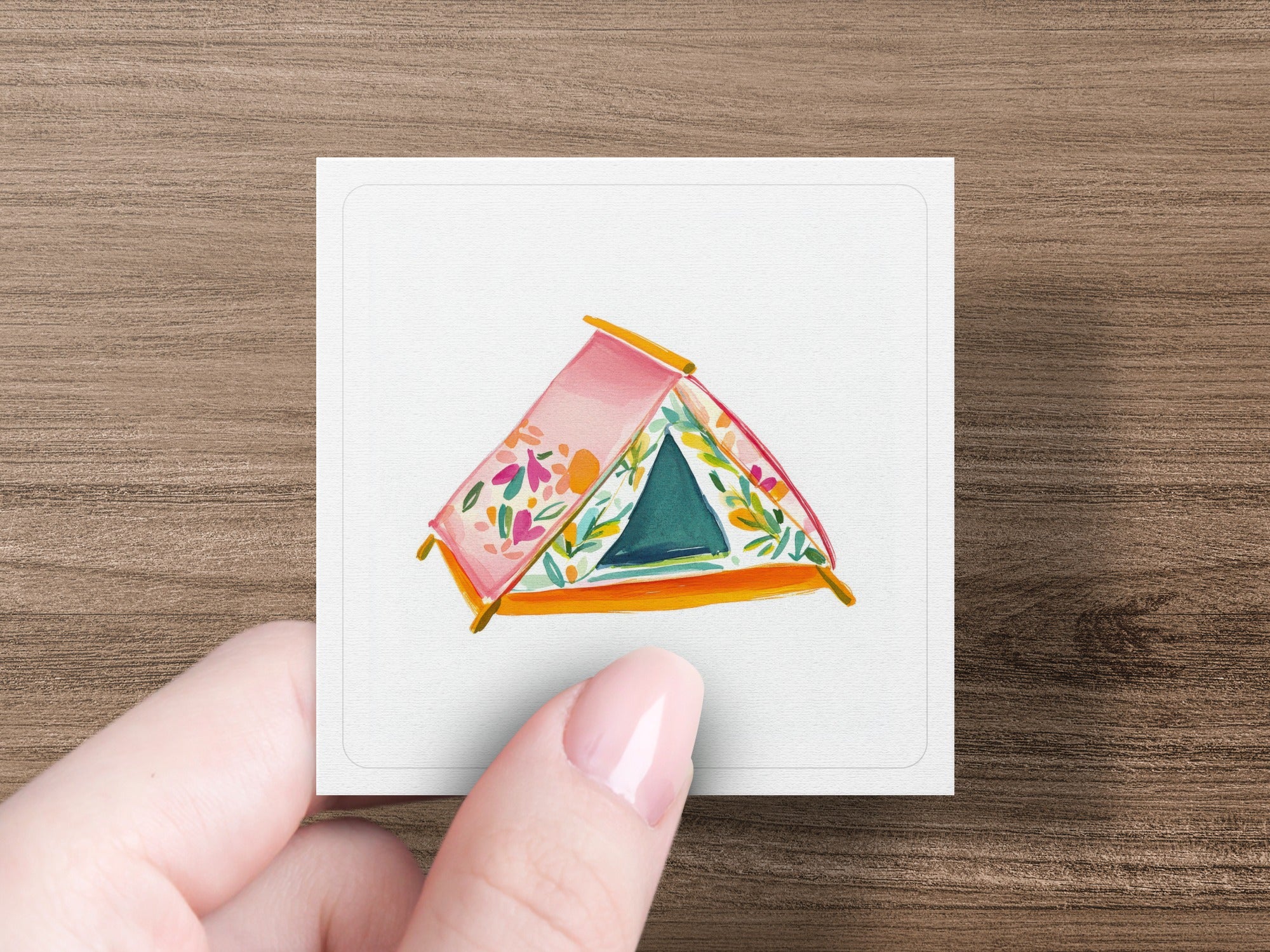 Pink tent with floral pattern and blue opening on white card held by hand.