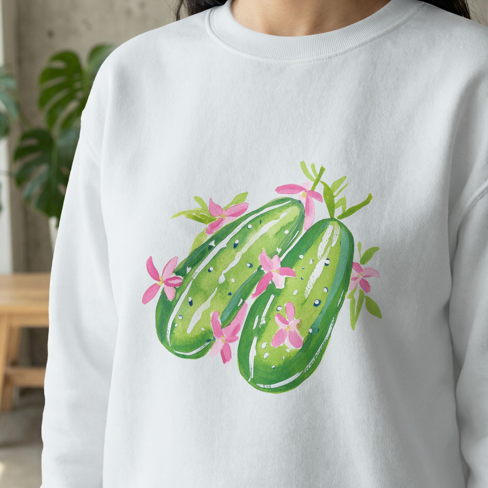 White sweatshirt with watercolor illustration of two cucumbers and pink flowers.