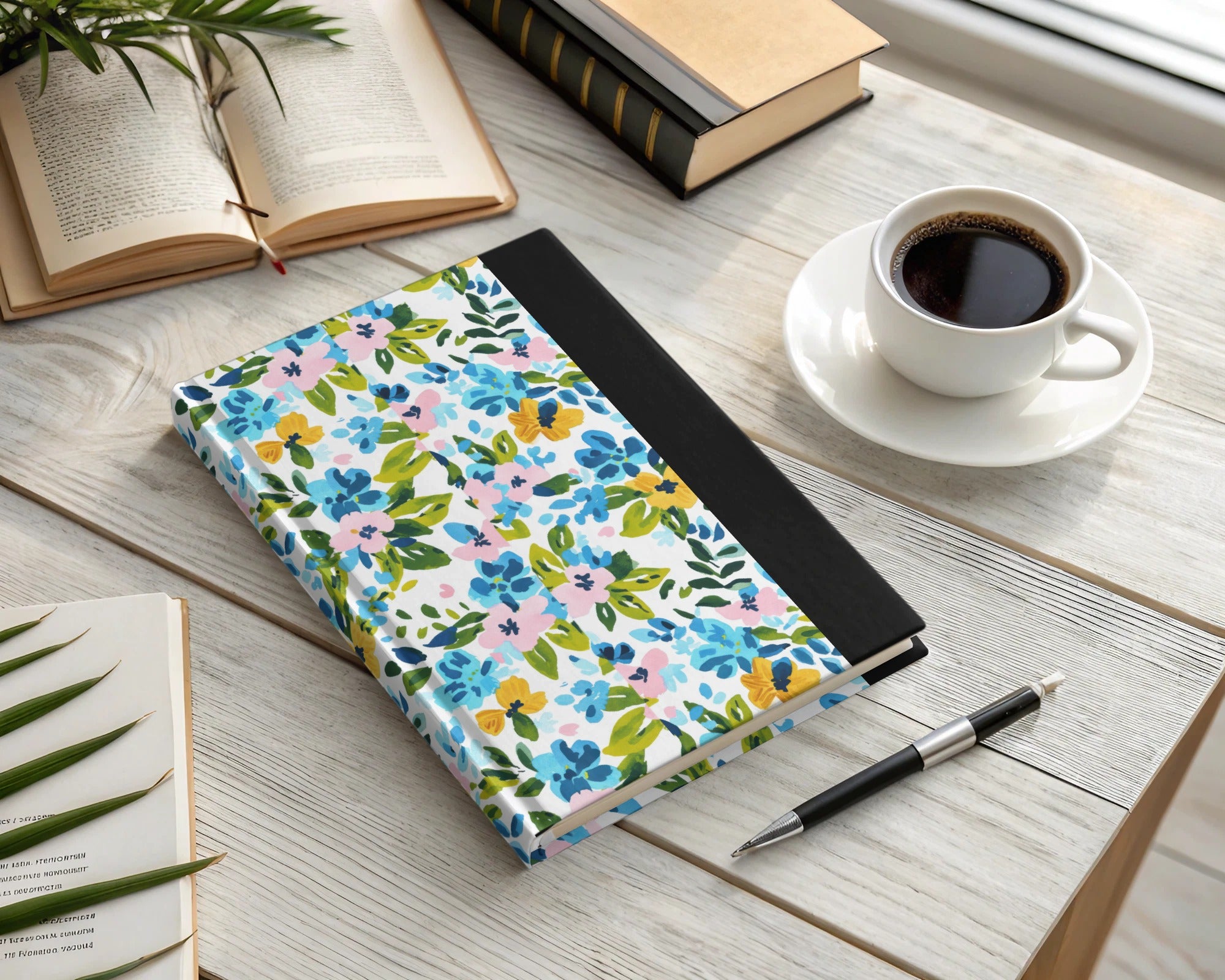 Floral patterned notebook with pen and coffee cup on a wooden desk.