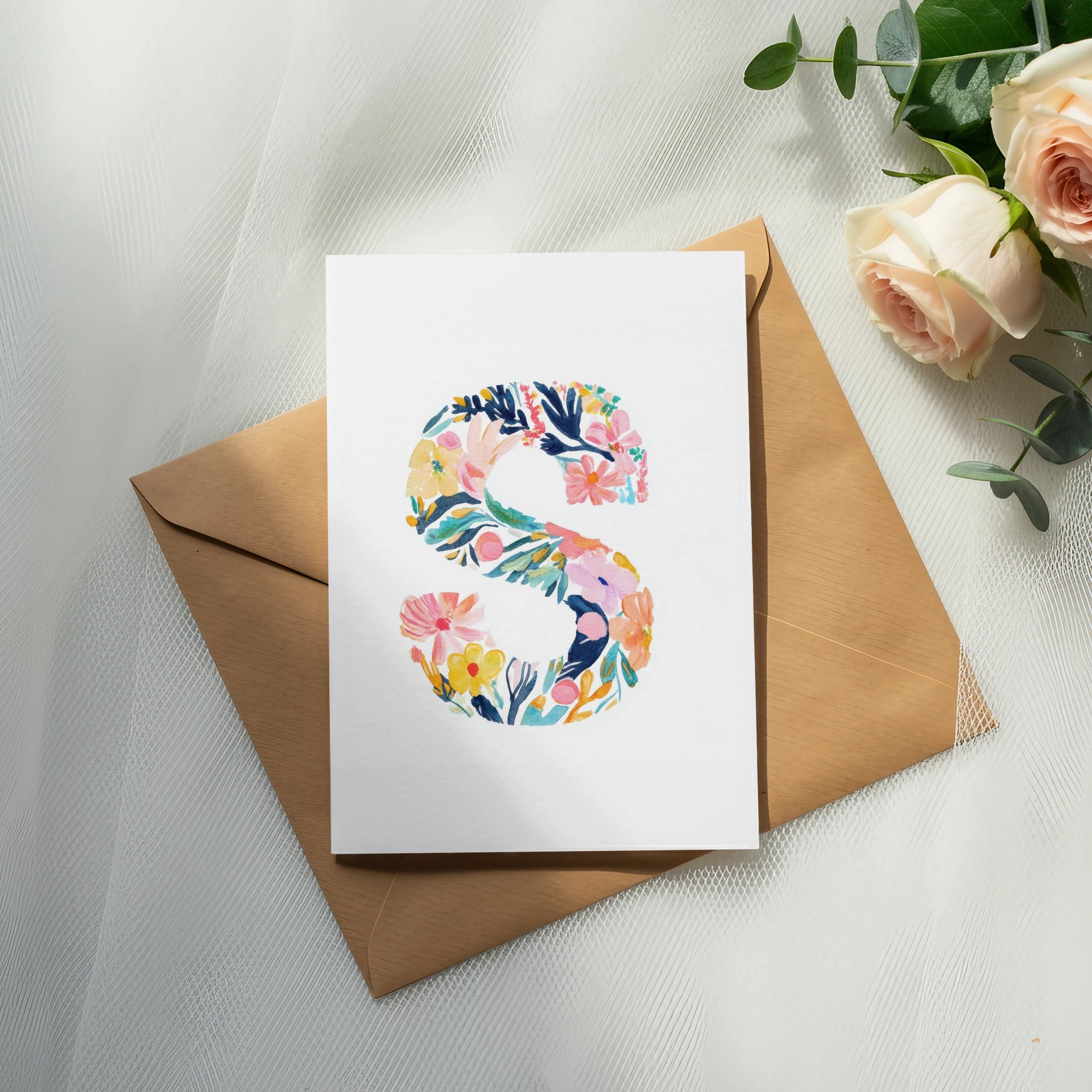 Card with floral letter "S" on a brown envelope, with roses and eucalyptus.